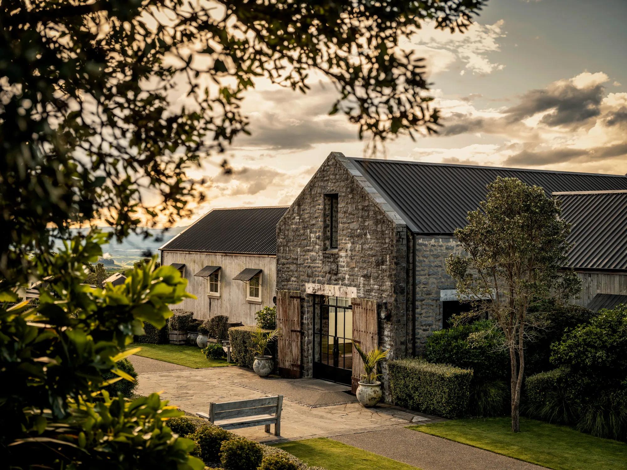 Stone hotel building with metal roof, landscaped gardens, and walkway at sunset.