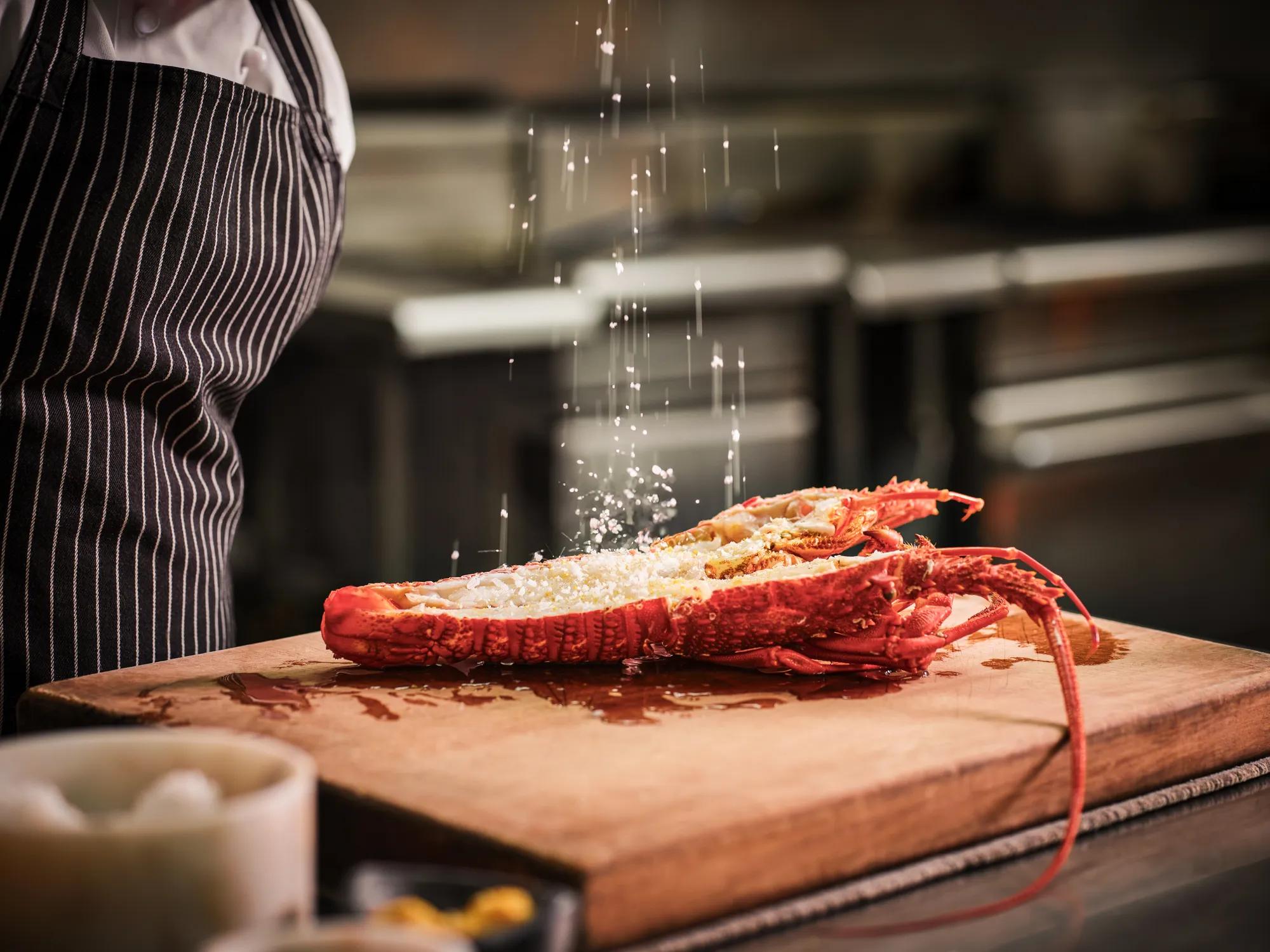 Two fishermen from Tora Collective on a boat collecting crayfish out of a metal crayfish pot.