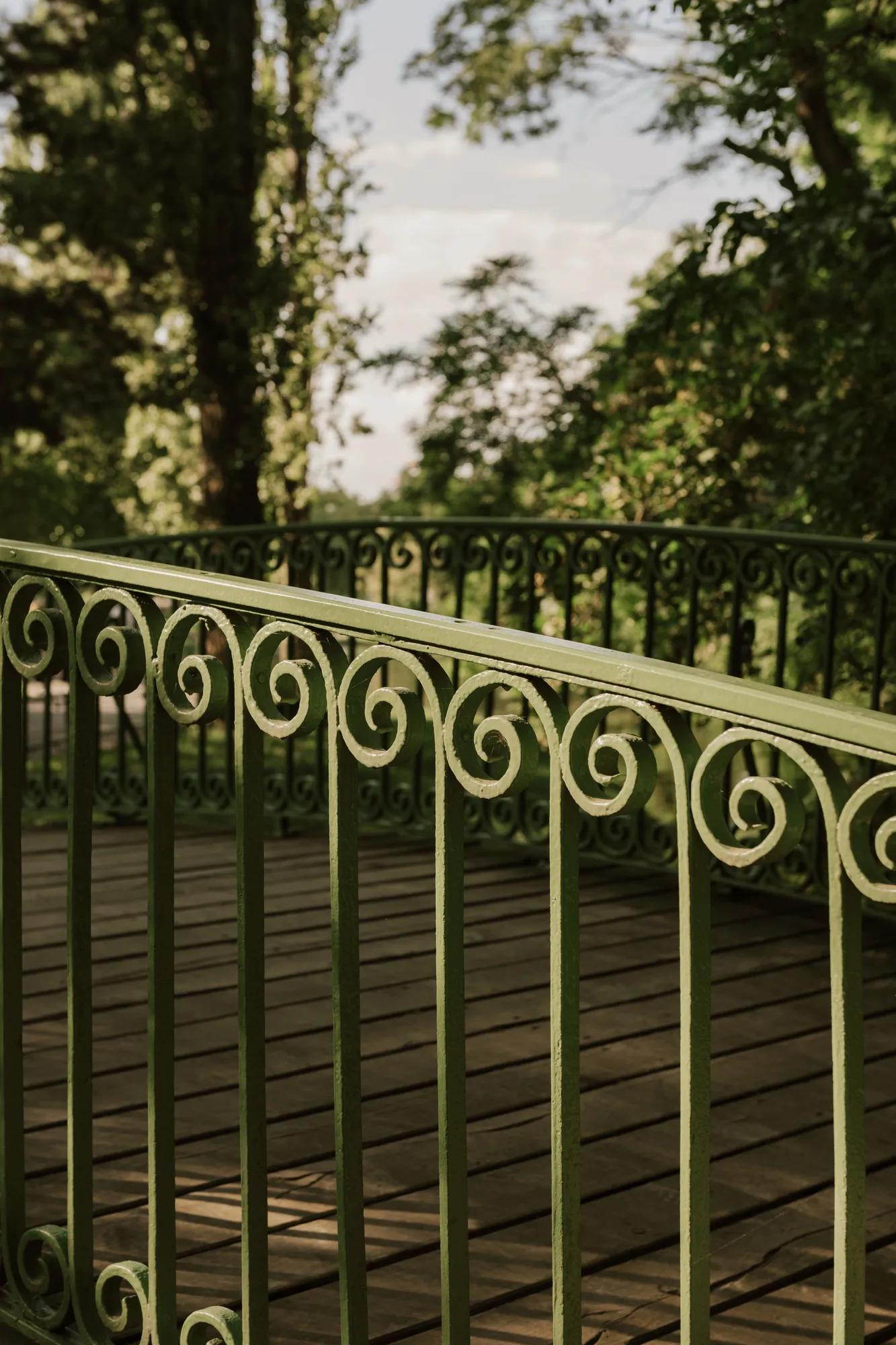 Ornate green iron railing of the Konstantinsteg bridge at Vienna’s Prater, surrounded by lush trees.