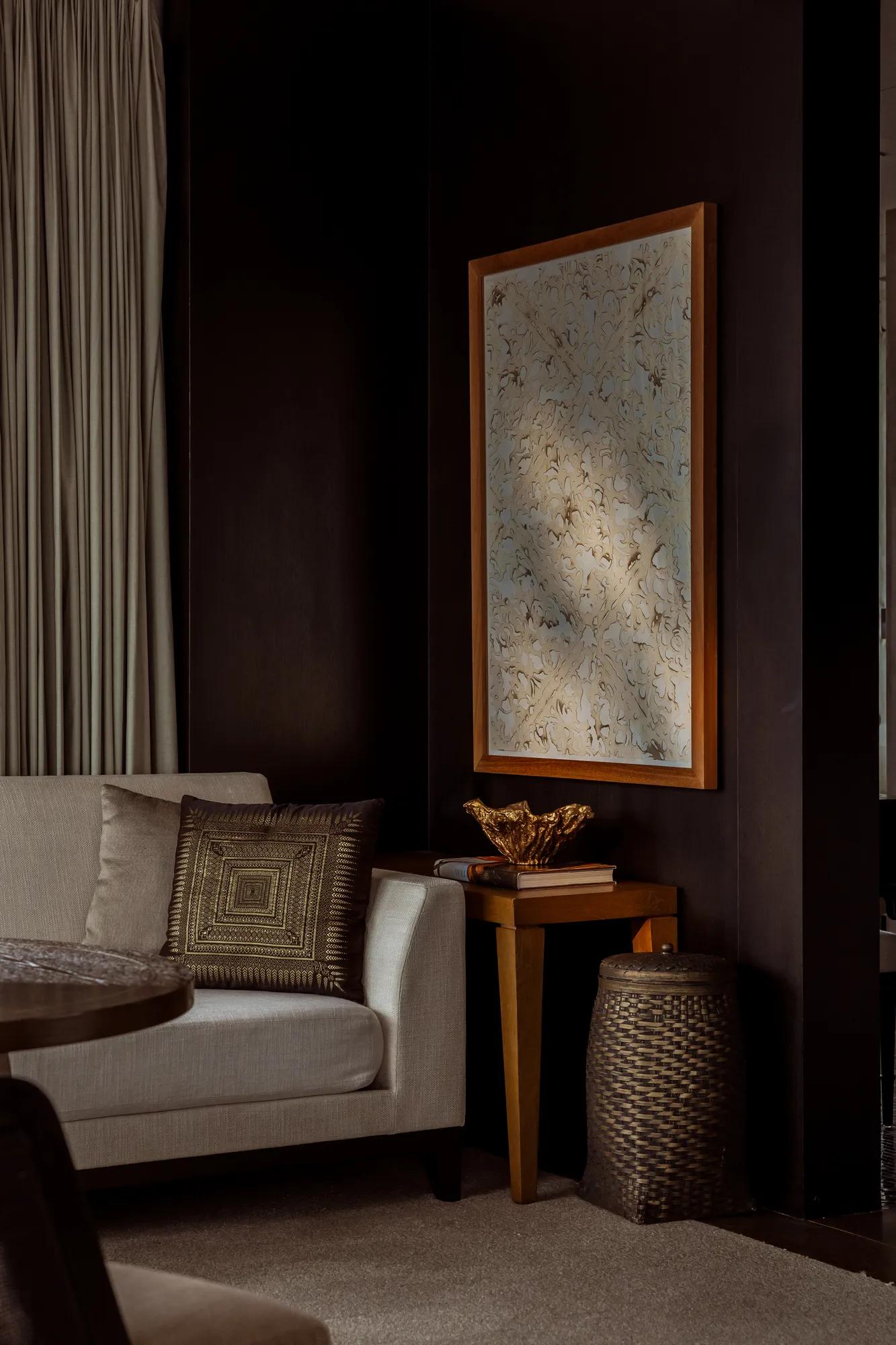 Dark hotel room in a Phnom  Penh hotel with a beige sofa  and botanical artwork. 