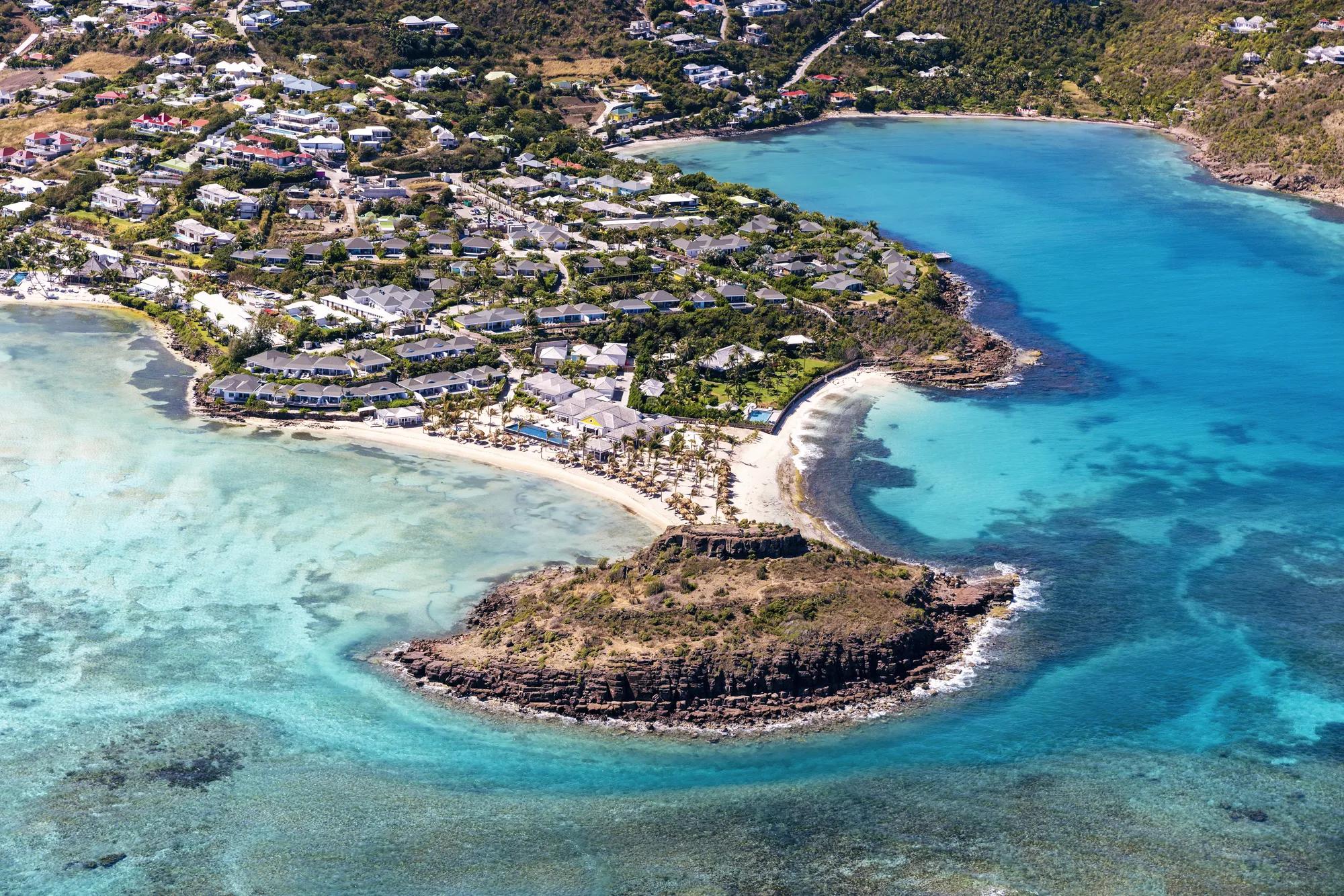St. Barth Beach with clear water, resort buildings, a mountain, and thatched umbrellas along the beach.