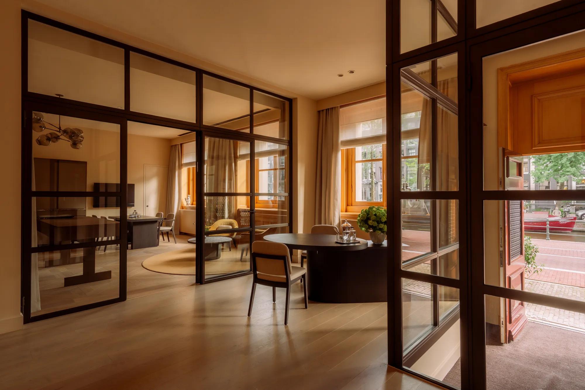 Furnished spaces separated in three by glass crittal doors. A door leading onto the street and canal is open. 