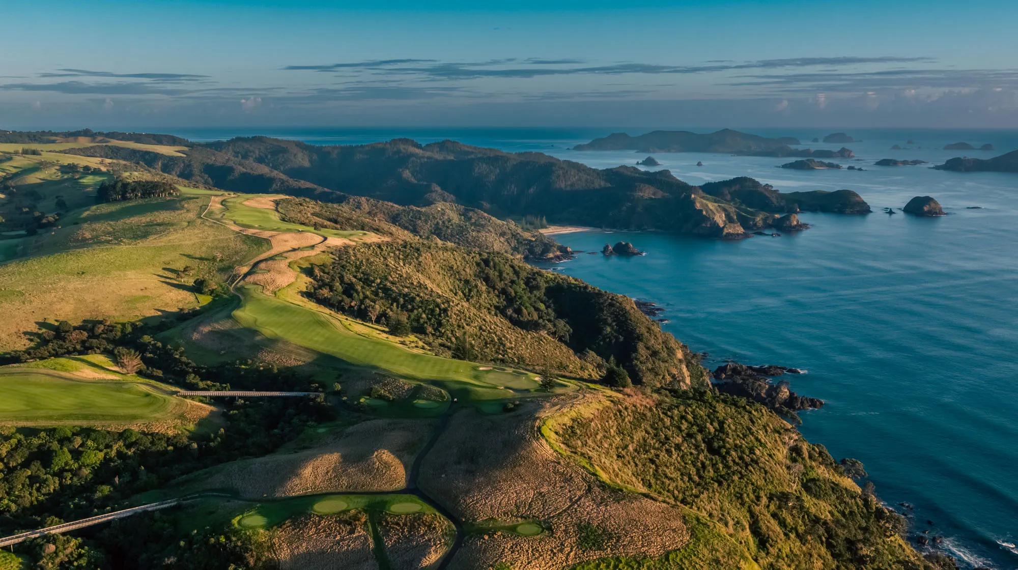 New Zealand golf course with rolling greens and dramatic cliffs overlooking the ocean and islands in the background.