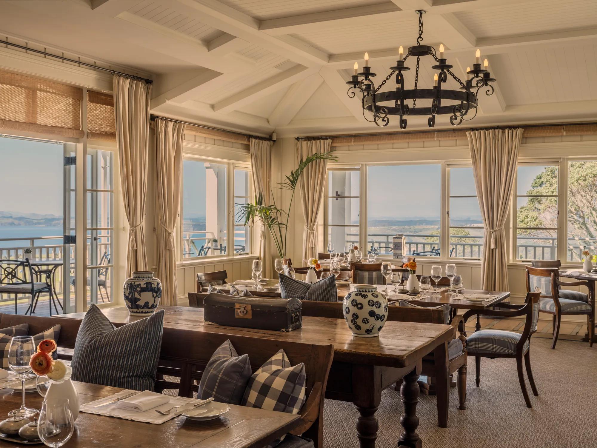 Set tables in the main dining room with the doors open to the main balcony and panoramic views out to the Pacific Ocean.