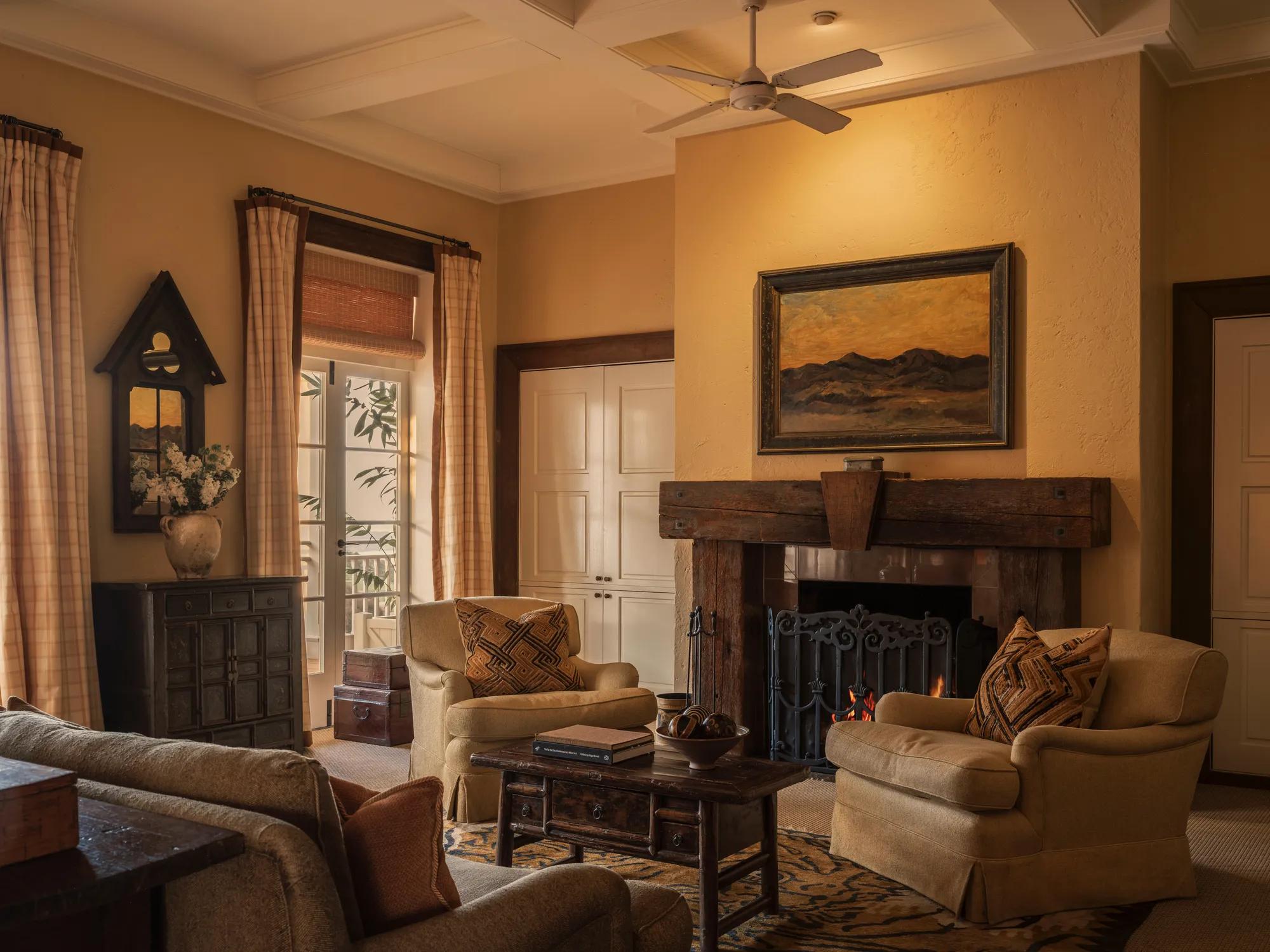 A warm and cozy room filled with plush couches and armchairs, with an open fireplace with rustic timber mantle and furniture