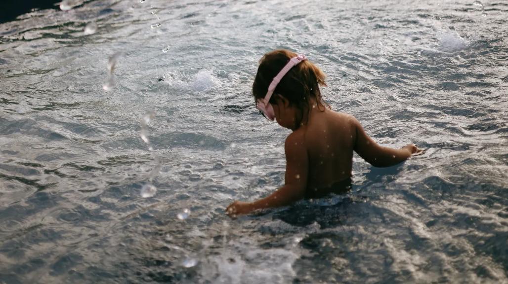 Boy chilld wearing a snorkling playing in the kids pool with the beach and palms in the distance. 