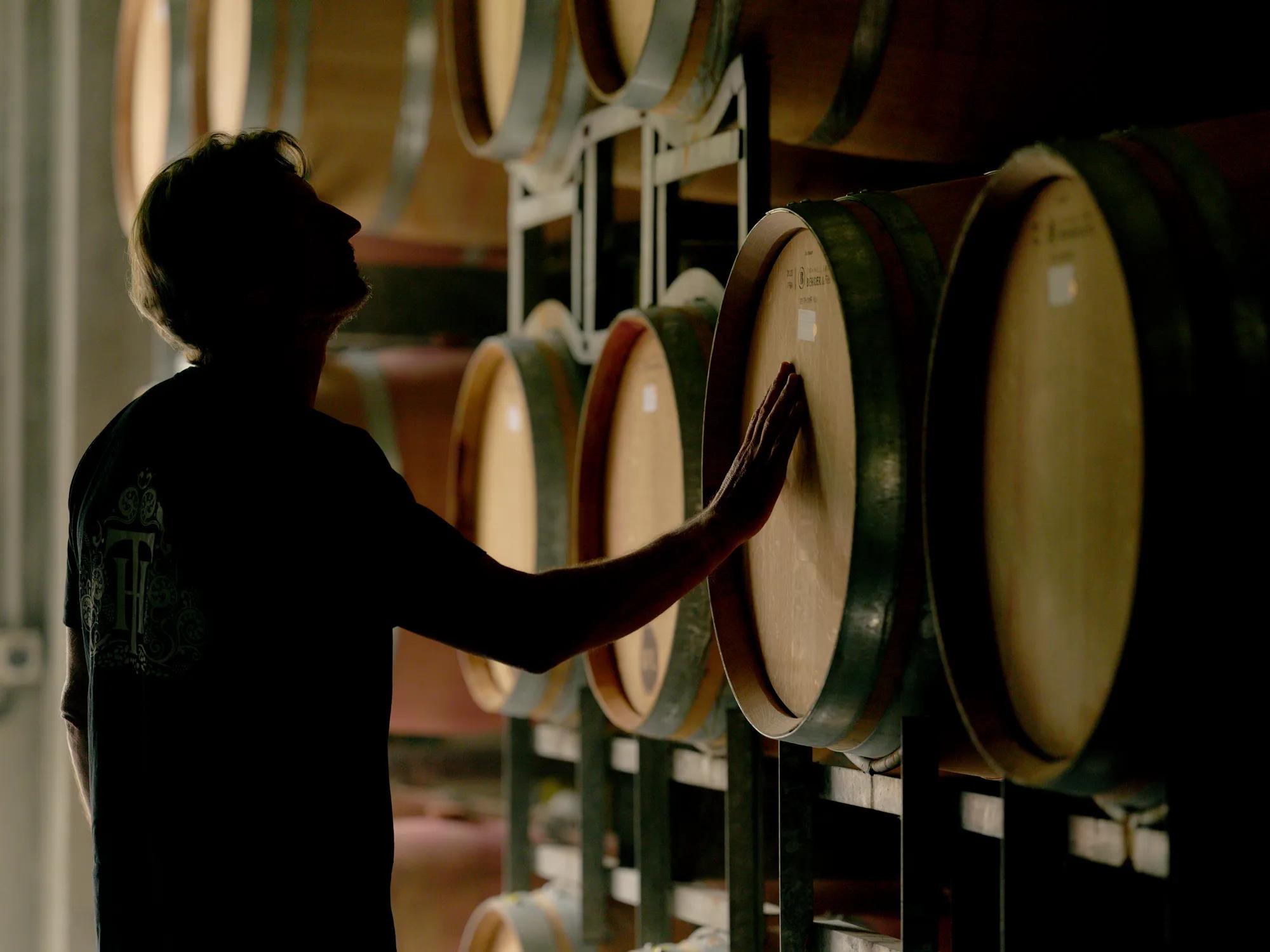 Wine maker at Trinity Hill touching and looking up at a wall of barrels.
