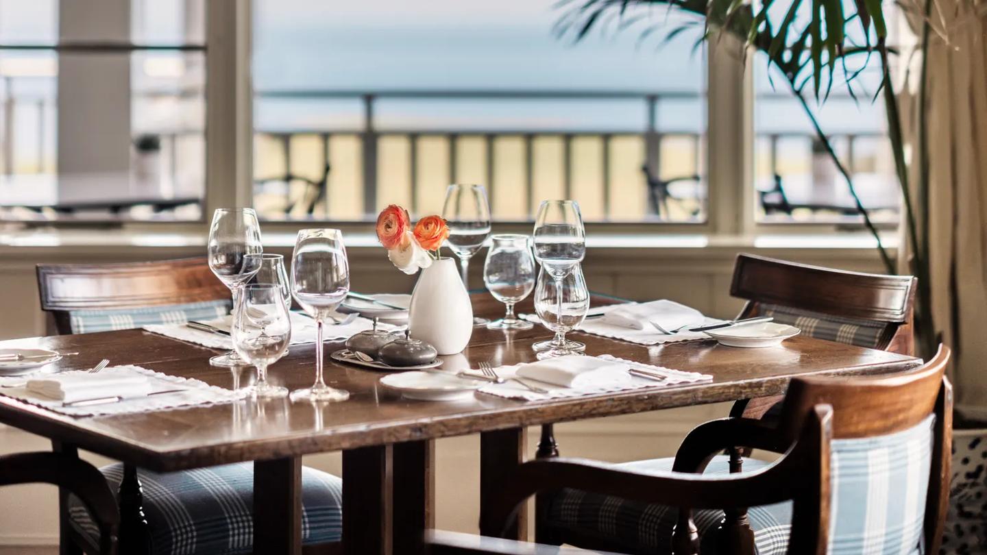 Beautifully set table in a dining room with classic interiors and big picture windows to the balcony and ocean. 