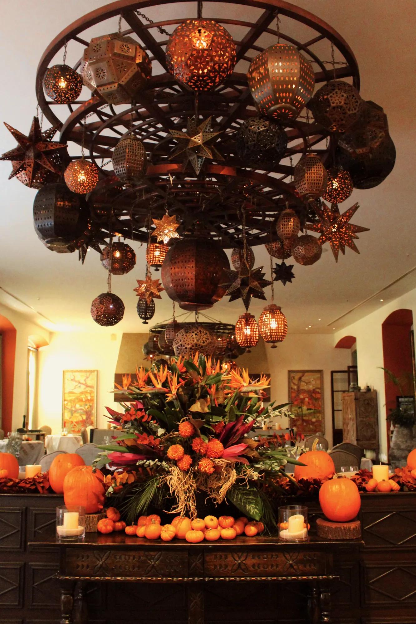 Thanksgiving table decoration with pumpkins, candles, and flowers on a restaurant table, featuring brass ornaments shaped like spheres and stars, typical of San Miguel de Allende.