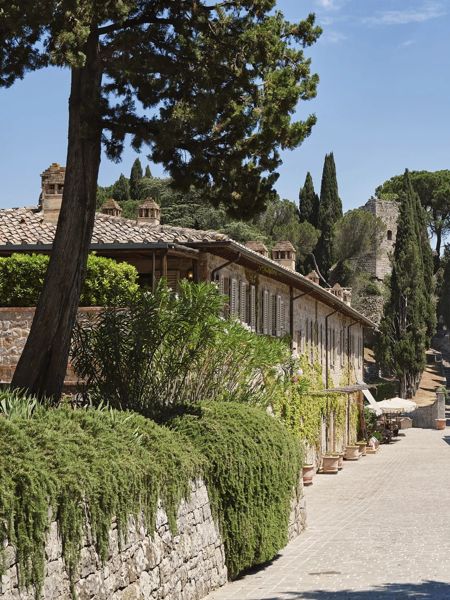 Sentiero in pietra in un resort in Val d’Orcia, circondato da cipressi ed edifici.