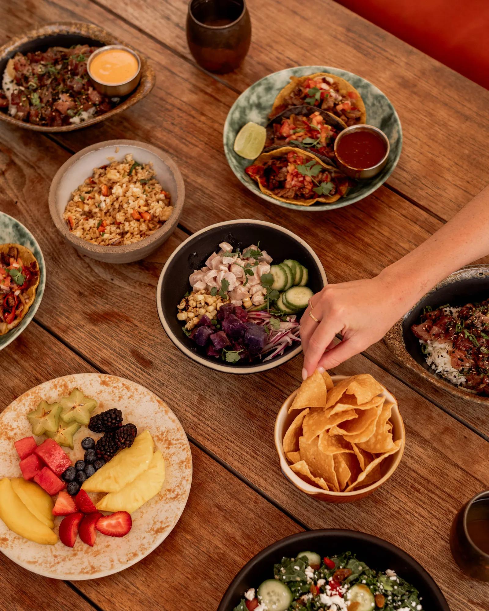 10 plates on a table with a person reaching out for a tortilla chip