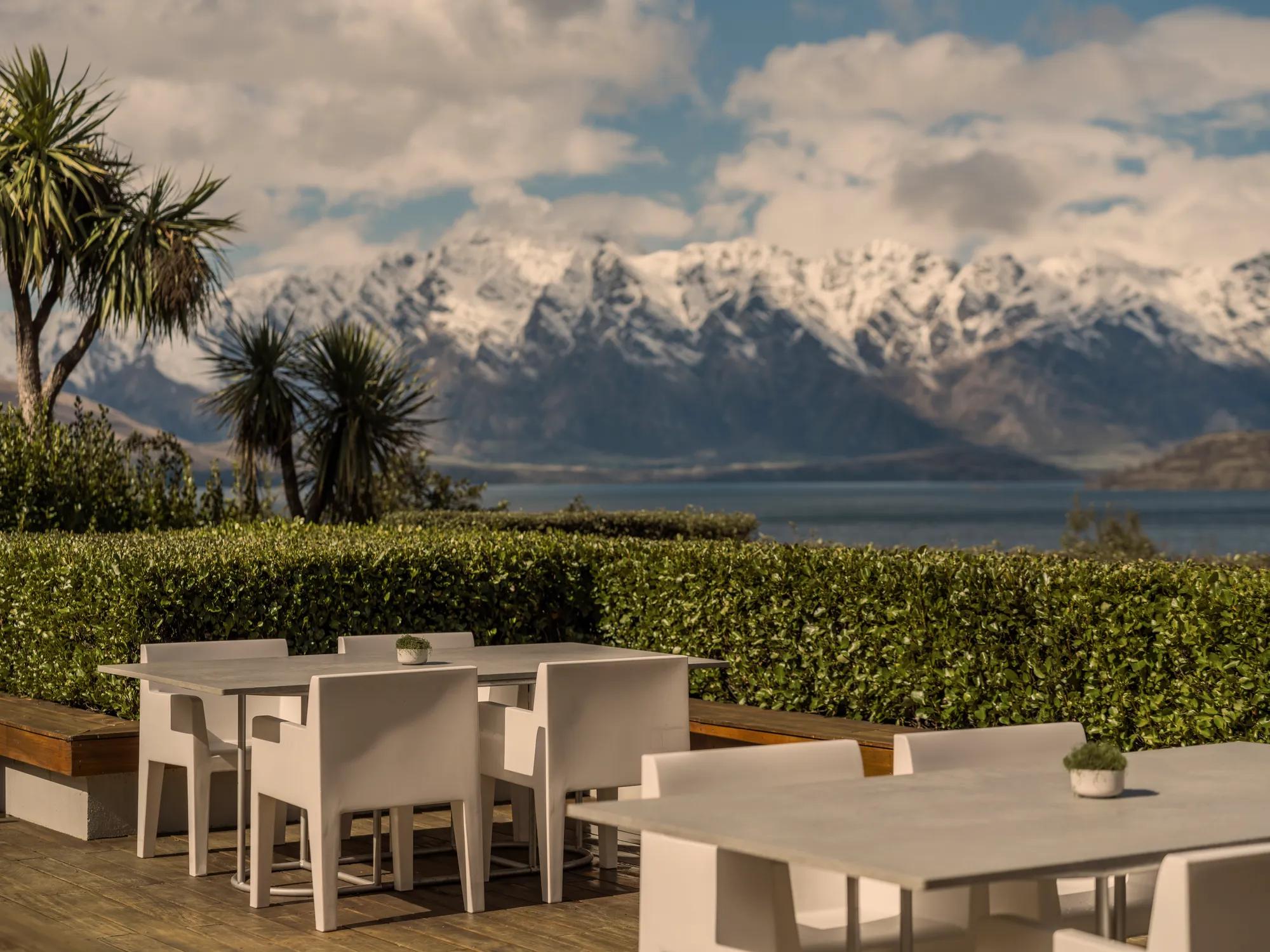 Two tables on the Remarkables Terrace with native plantings behind and stunning views of Lake Wakatipu and The Remarkables mountain range.