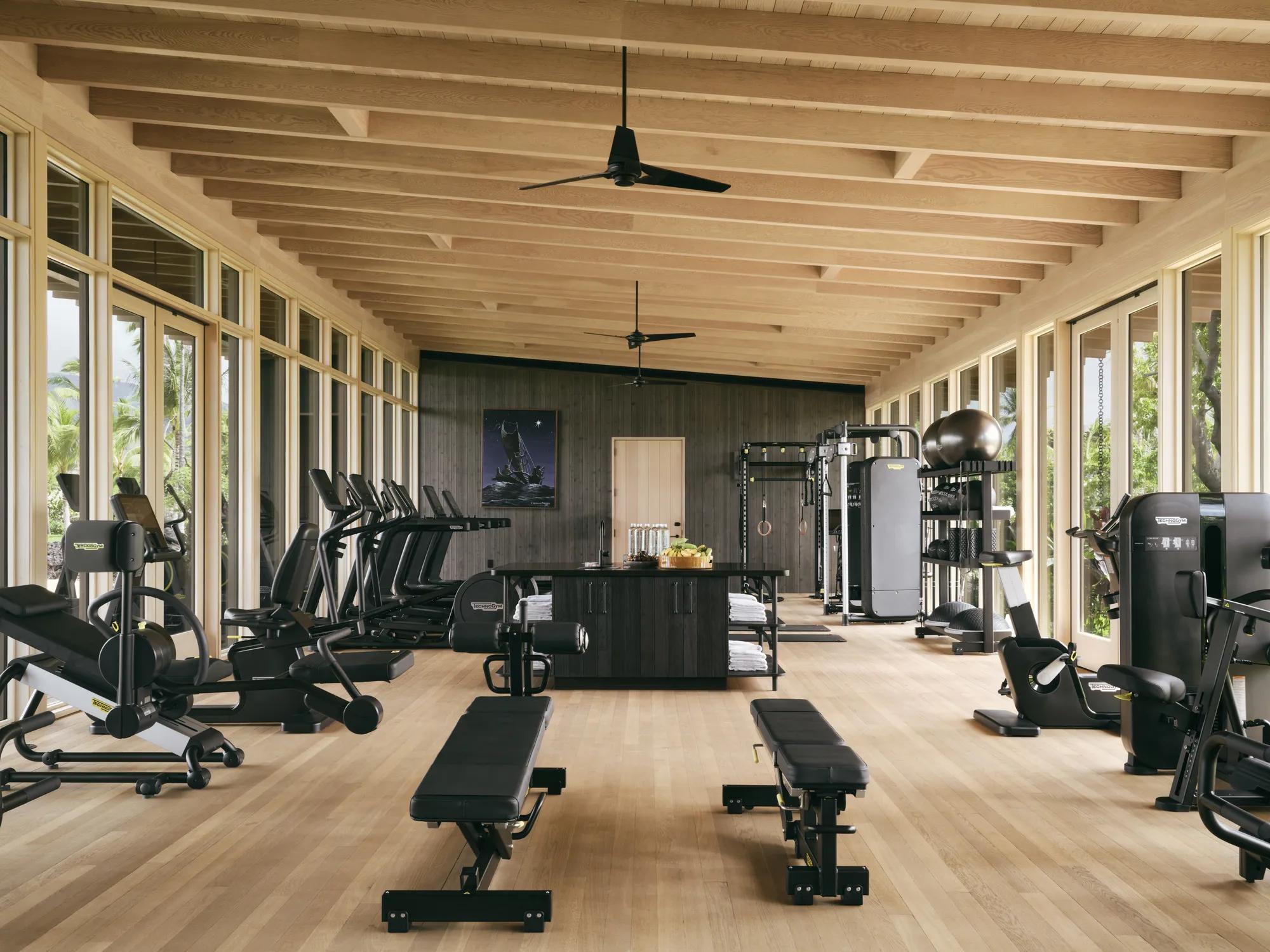 Wood paneled interior of a fitness center with cardio machines, workout benches, and a table with towels, bottled water and fruit.