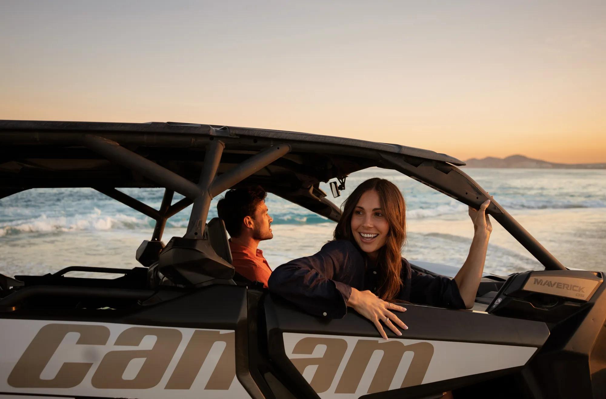 A couple riding a Razor off-road vehicle along the Sea of Cortez shoreline at sunset, with golden light reflecting on the water and sand