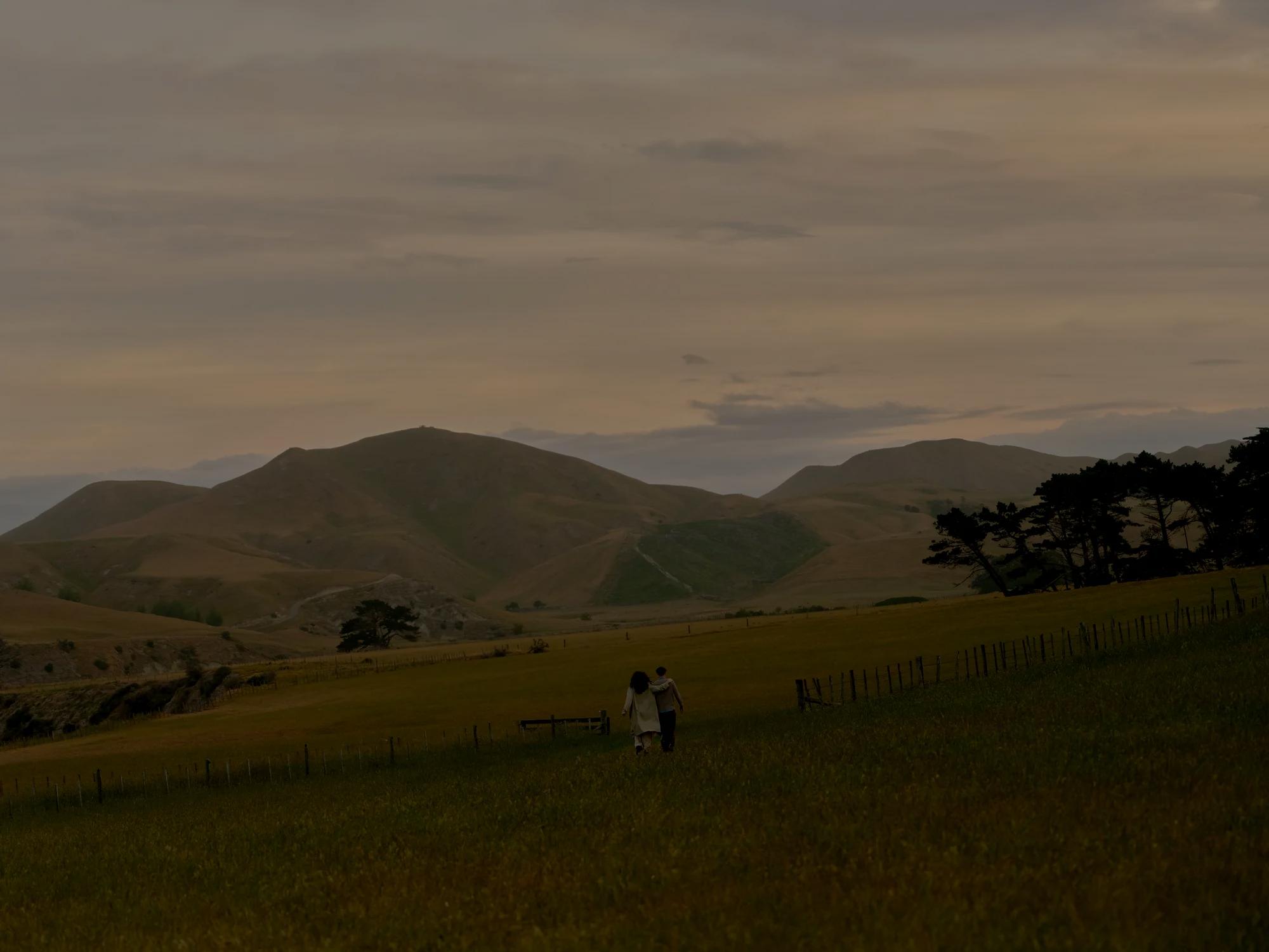 Couple walking in countryside setting with rolling hills in the distance.