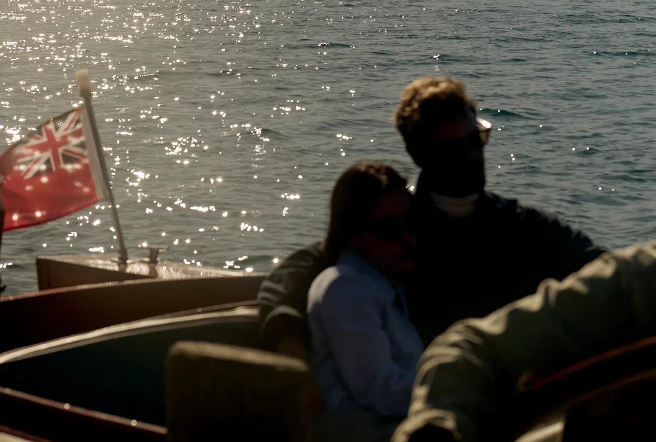 Couple snuggle up in the back of a vintage speedboat on Lake Wakatipu with The Remarkables mountain range visible in the distance.
