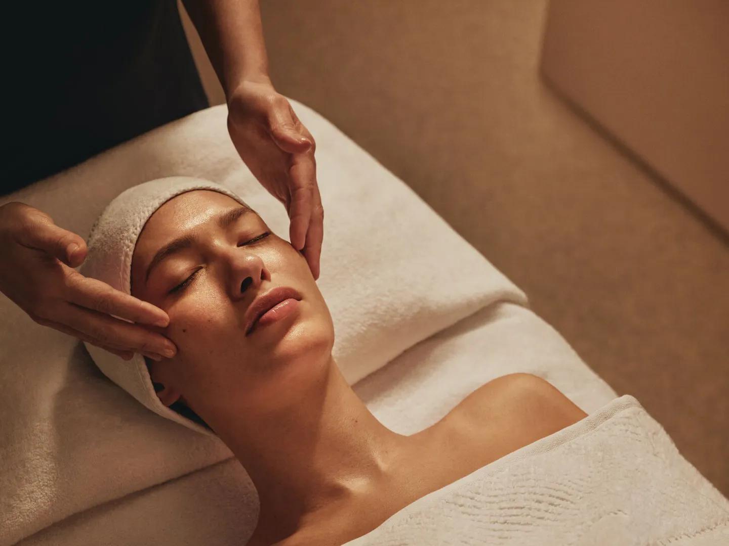 Spa therapist gently massages a clients face during a facial treatment.
