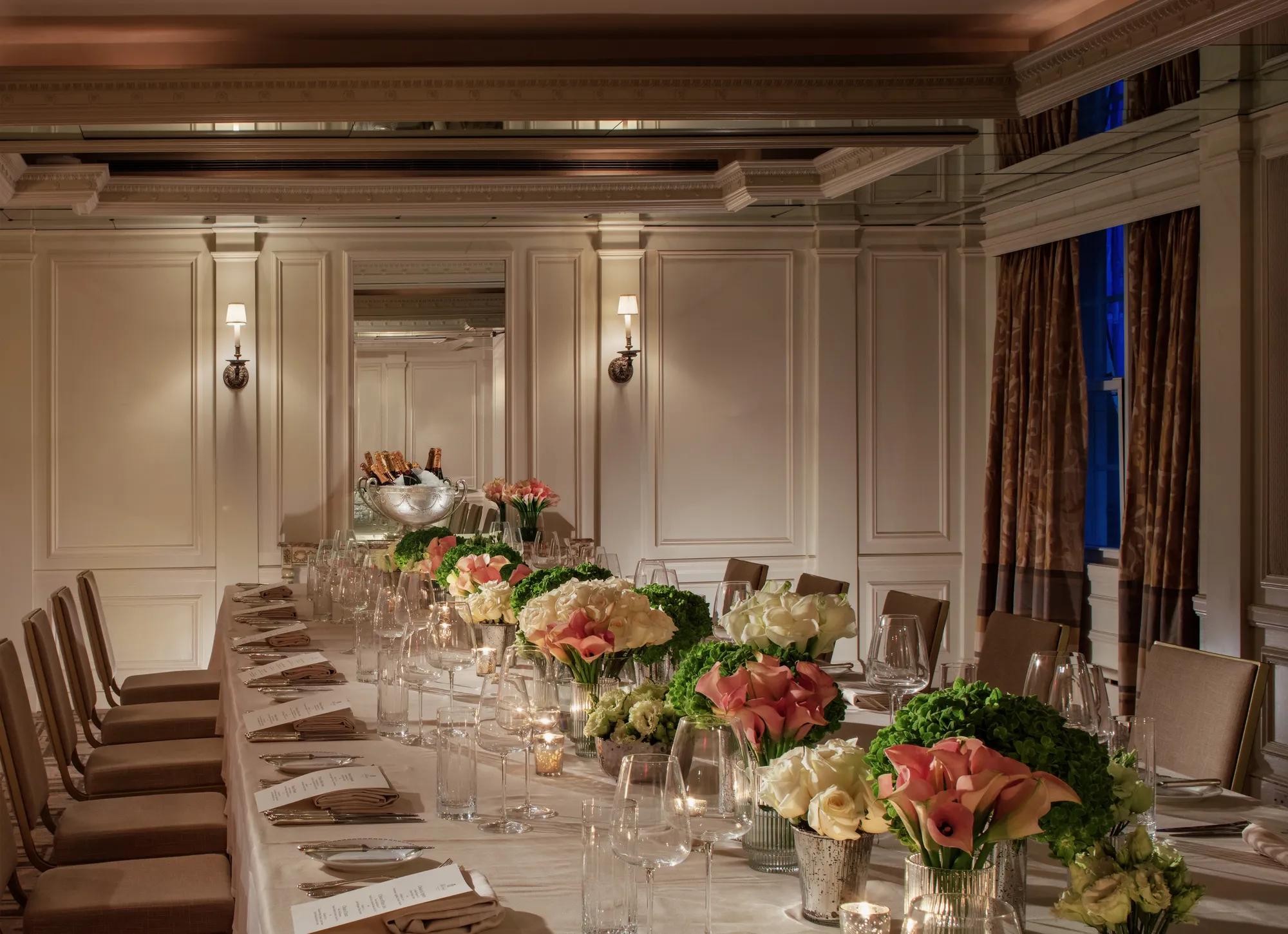 A banquet hall at The Carlyle with a long table decorated with plateware and florals. 