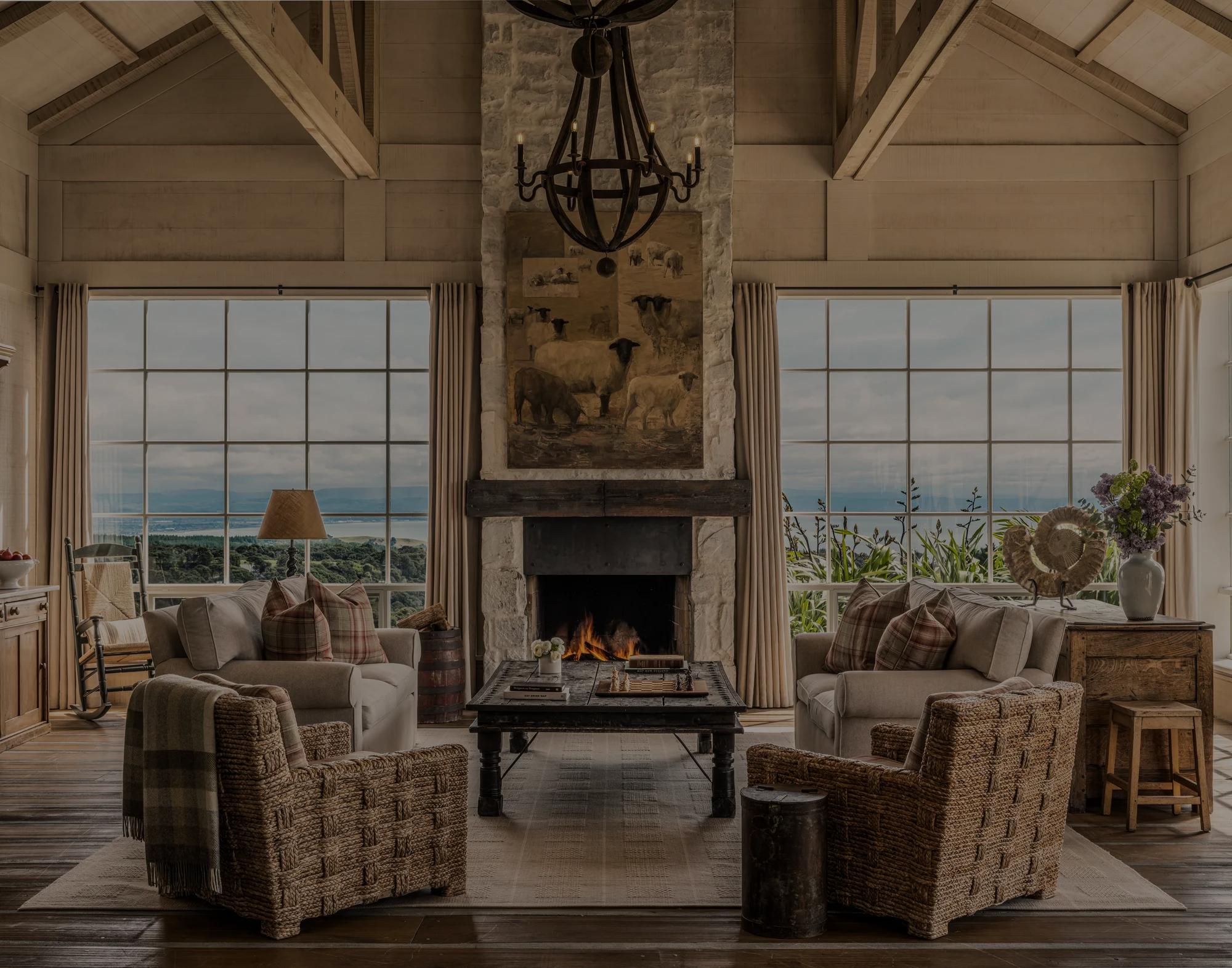 Living room in the Hawke’s Bay Four Bedroom Villa with refined countryside interiors, open fire, pitched ceiling and big windows to the views beyond.