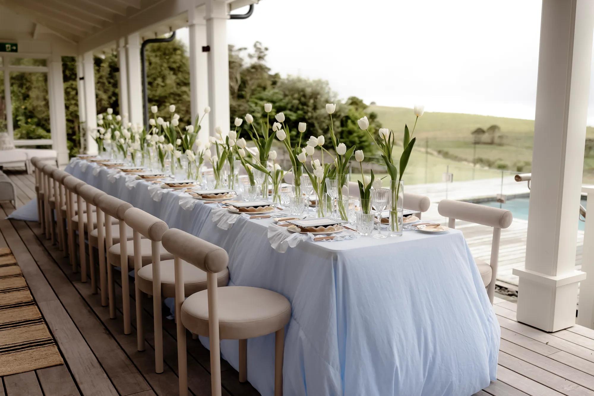 Beautifully set dining table with white tulips and blue linen tablecloth. 