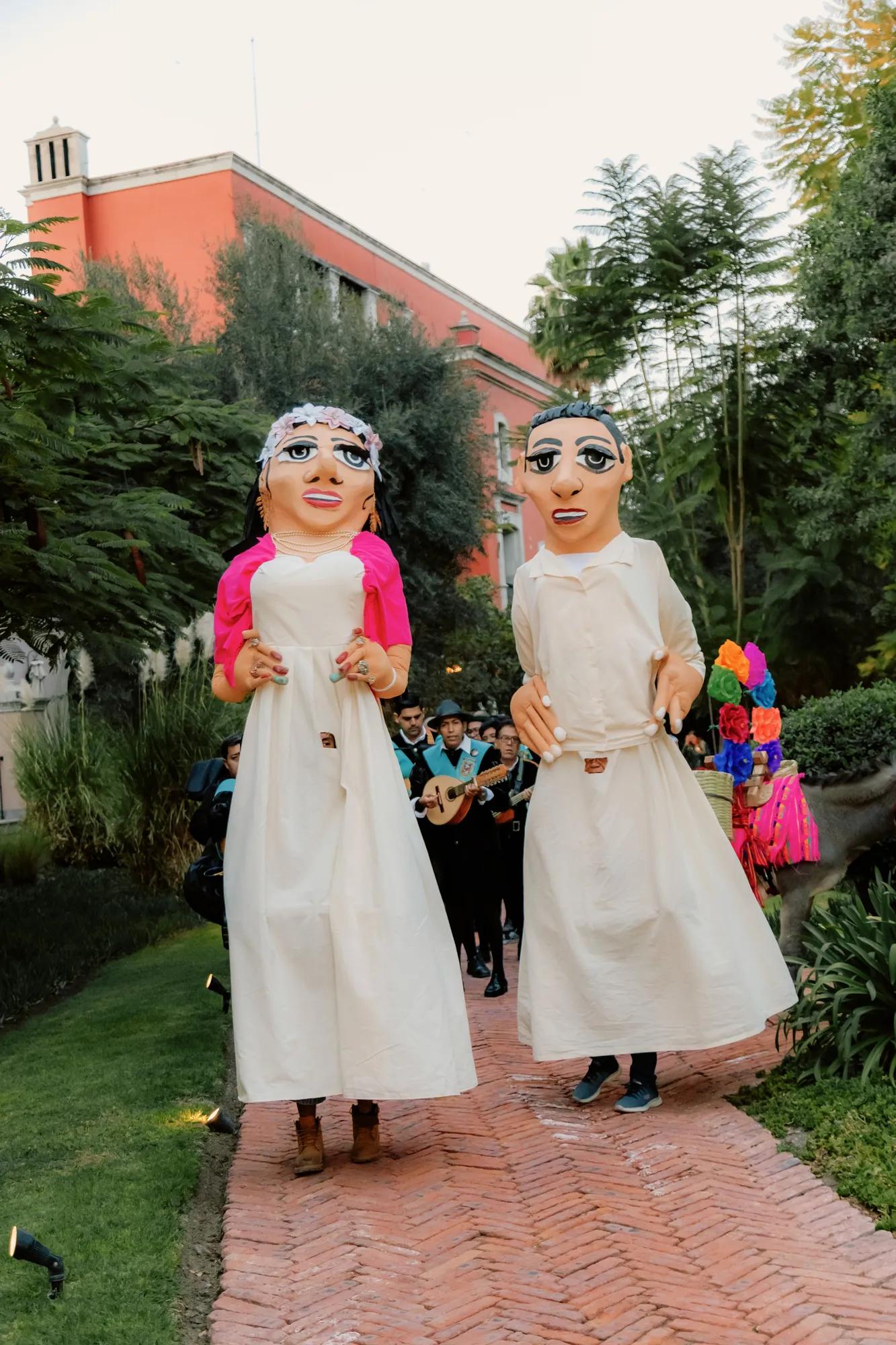 Traditional mojigangas parading along a garden path during a callejoneada in San Miguel de Allende.