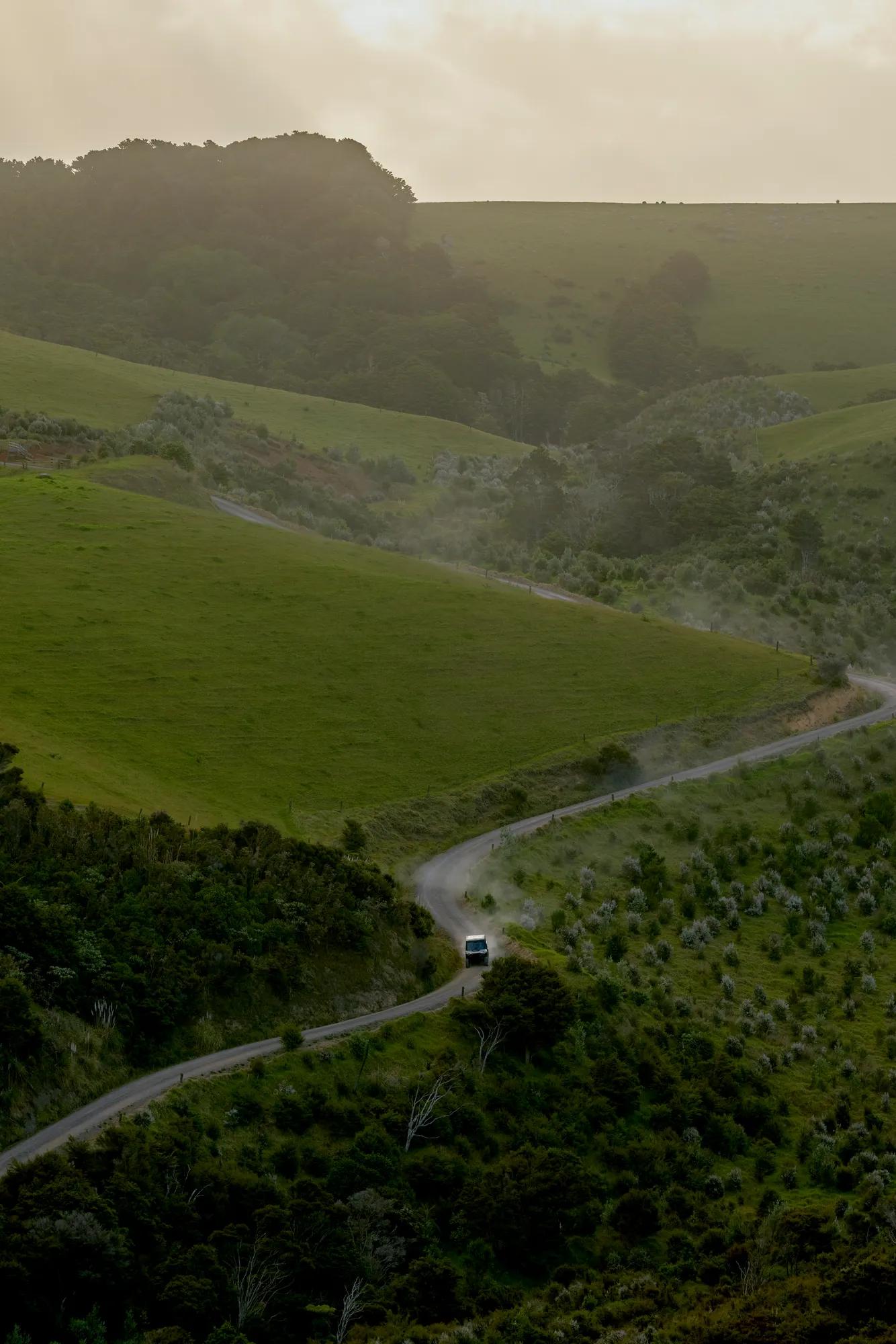Can-Am ATV vehicle travels down a secluded road surrounded by native bush and rolling green hills