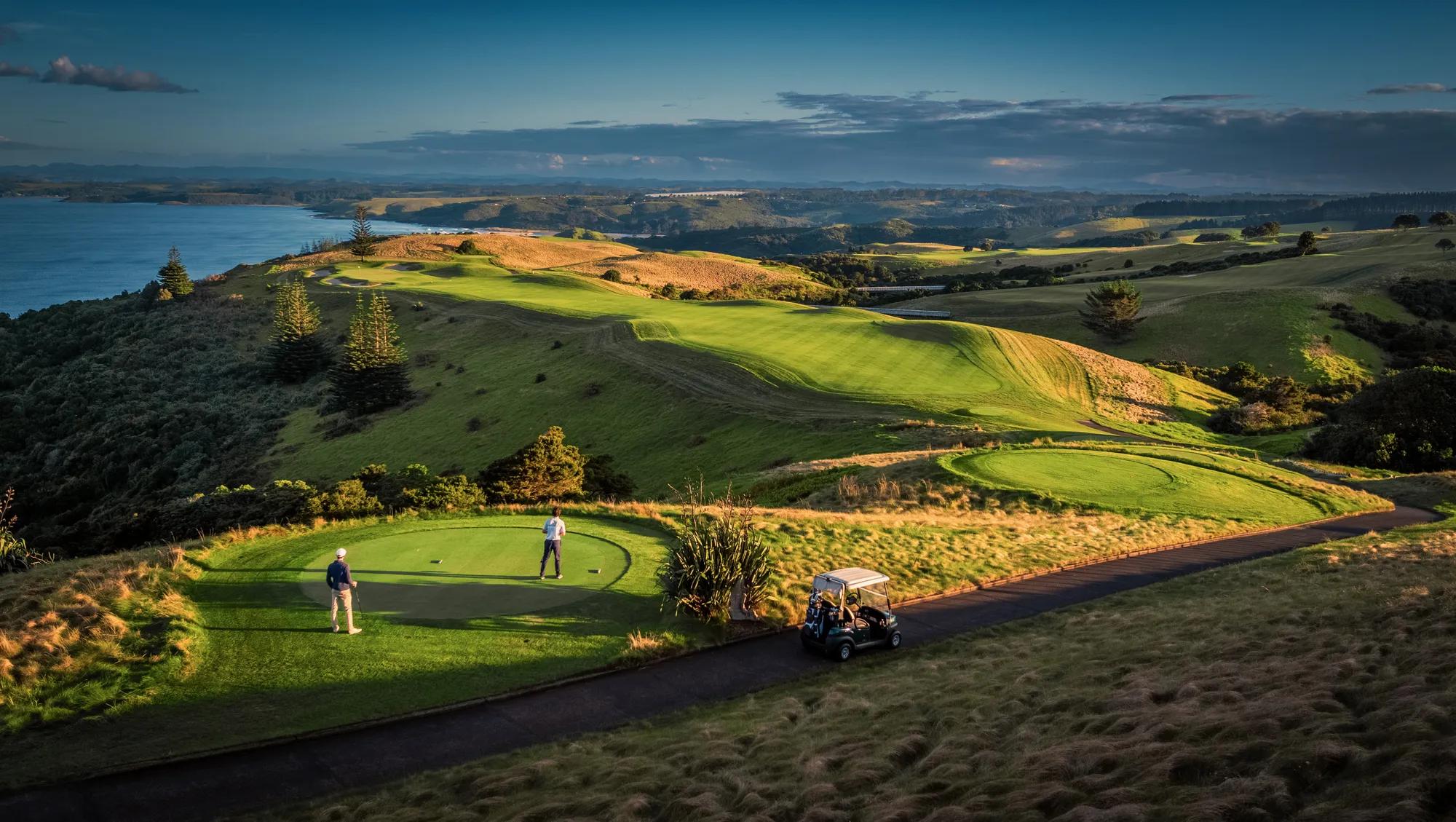 two golfers on the tee box looking out over the expansive Kauri Cliffs golf course