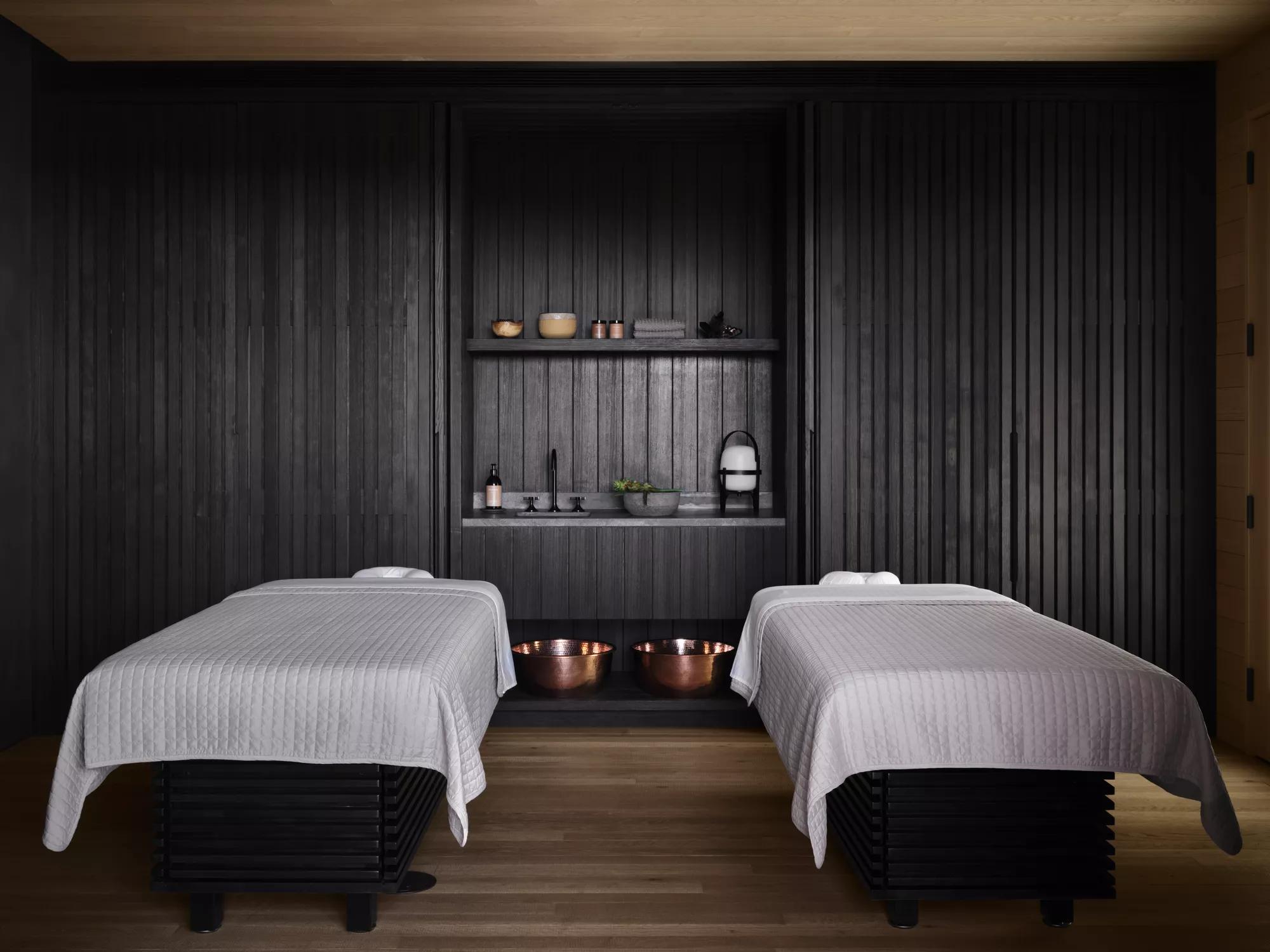 A spa treatment room with dark paneled walls and two massage tables