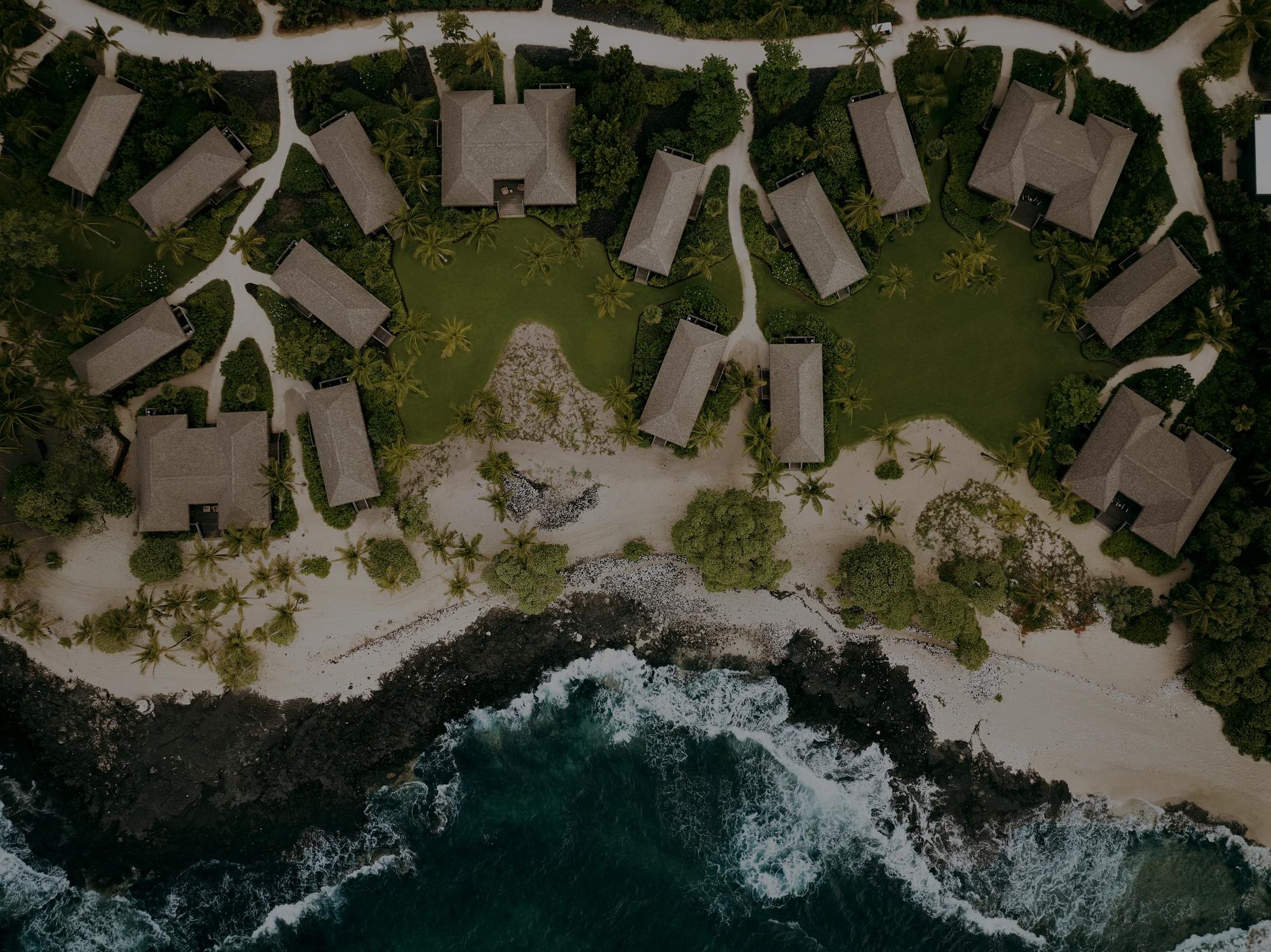 Overhead view of bungalow buildings and grass lawns at the shote with ocean waves crashing against lava rock 