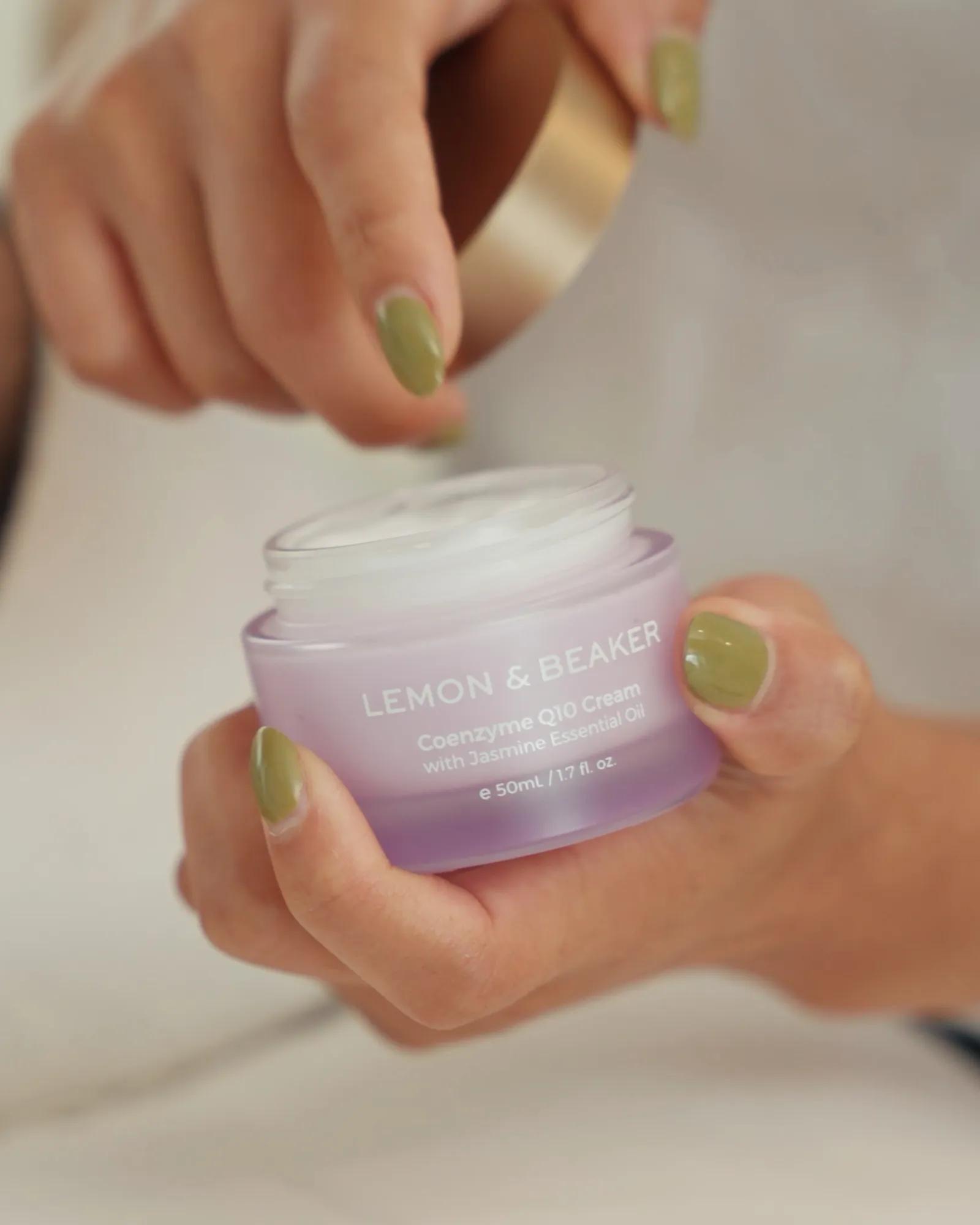 Close-up product lifestyle shot of a woman holding Lemon & Beaker face cream before application.