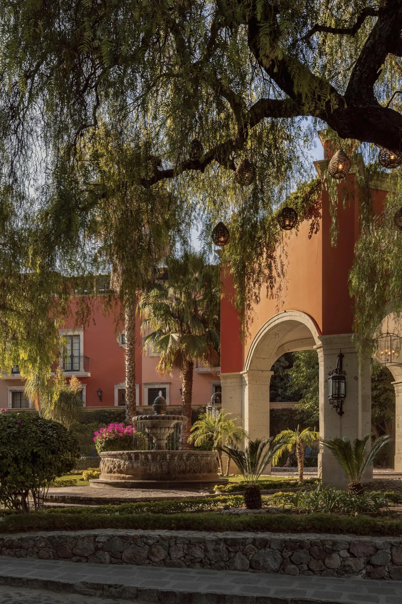 A stone fountain in the motor lobby with a large tree overhead adorned with hanging lantern spheres, and the hotel façade in the background. 