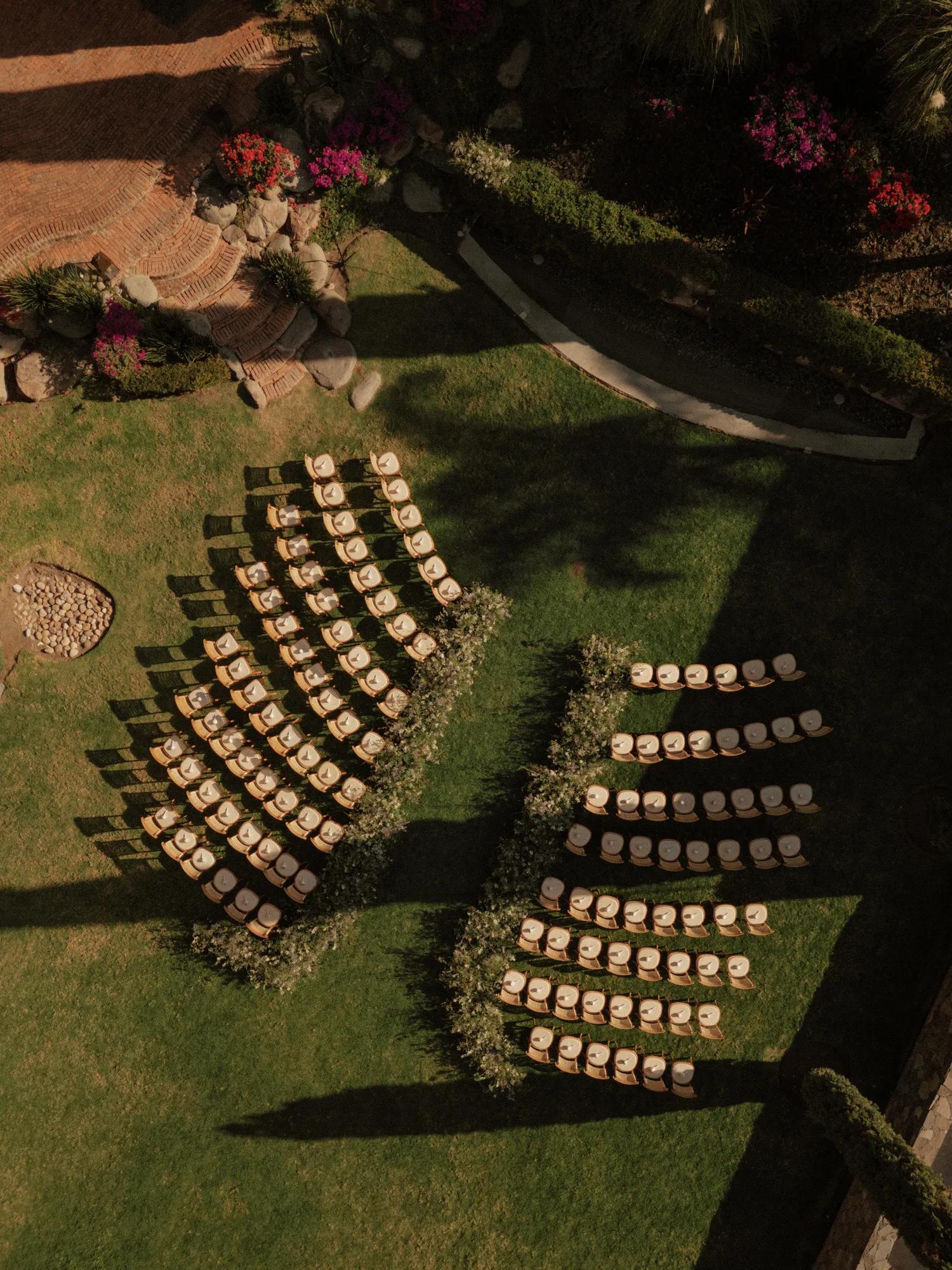Outdoor garden ceremony setup on a grassy lawn, with rows of chairs facing a natural backdrop of lush greenery.