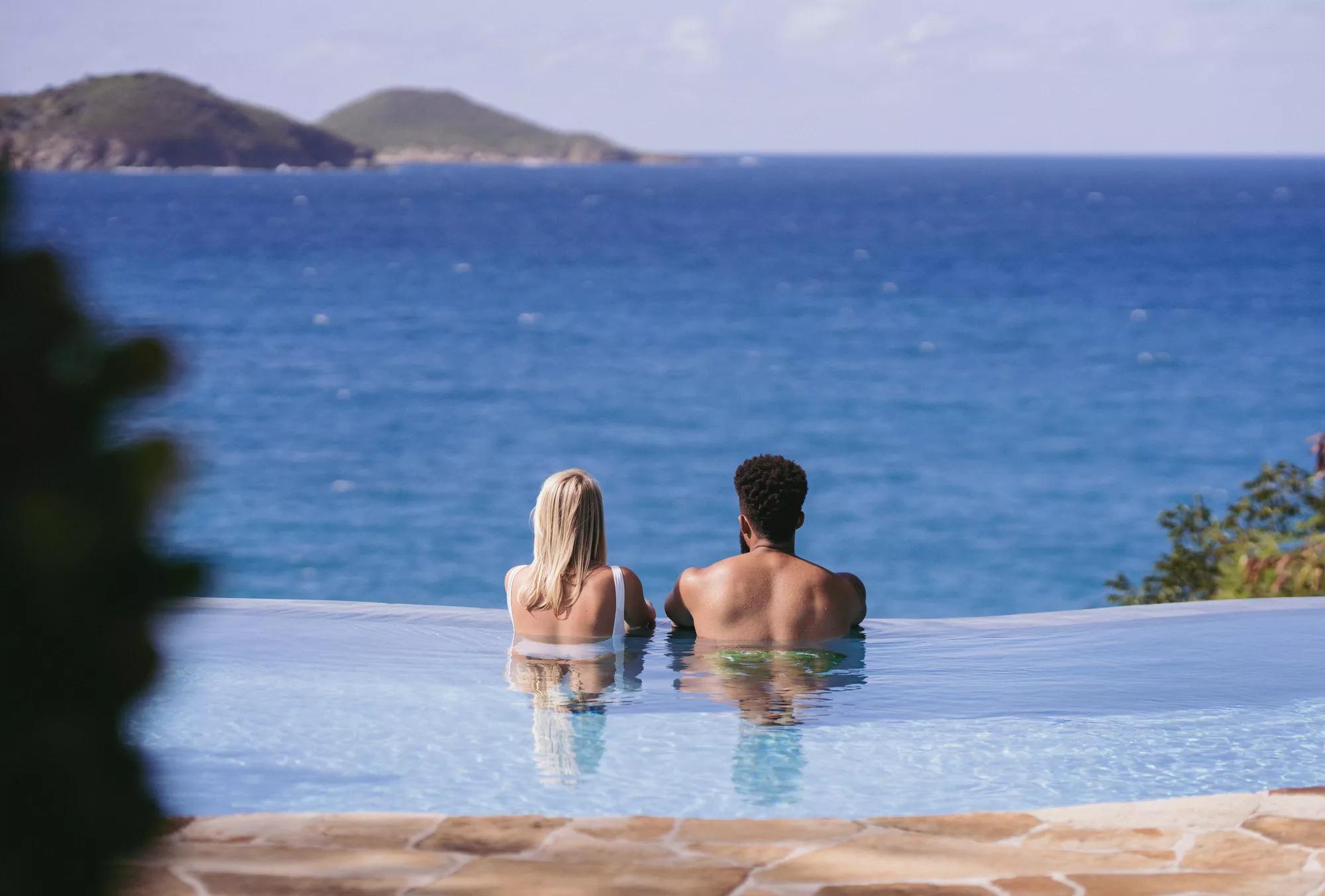 Outdoor pool with stone tile walls surrounded by palm trees and tropical gardens.