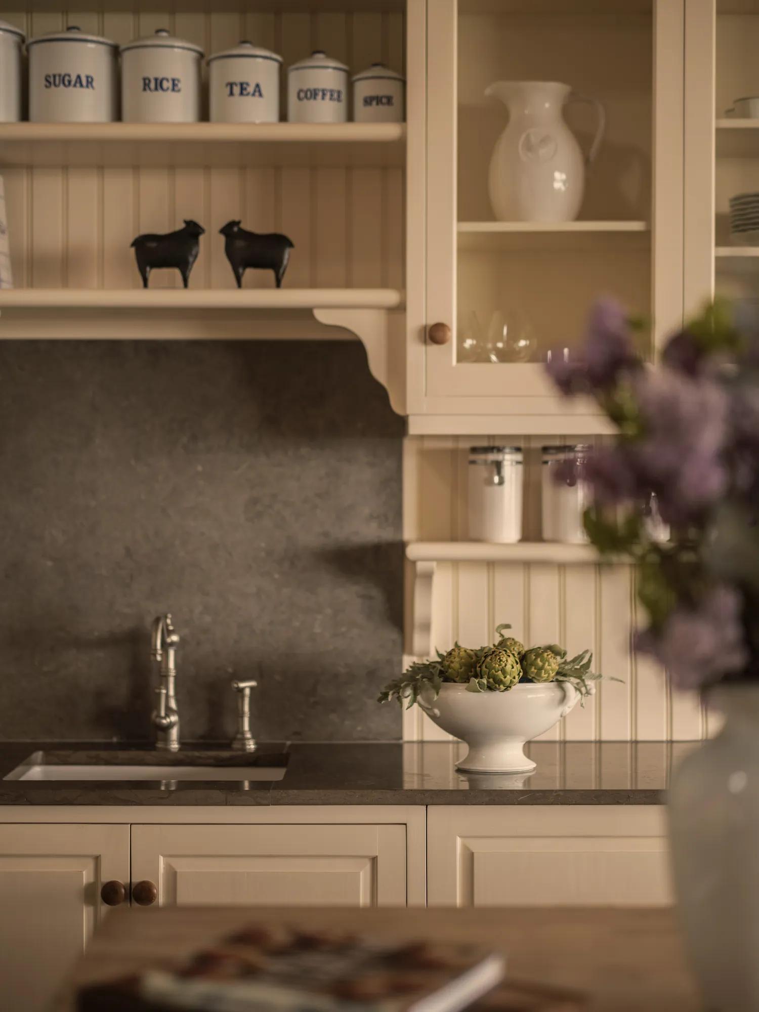 Farm style kitchen in a luxury villa with purple flowers out of focus in the foreground and a bowl of fresh artichoke in the background.