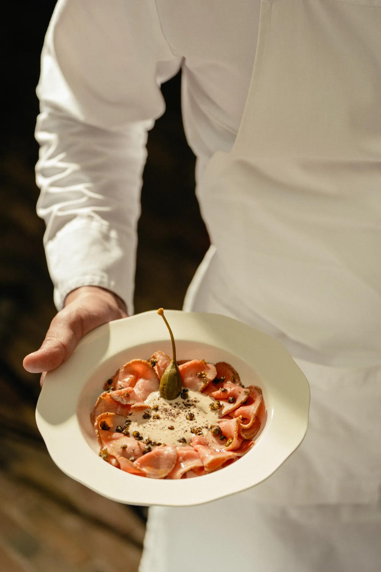 Vitello Tonato on a plate in the hand of the chef presenting the dish
