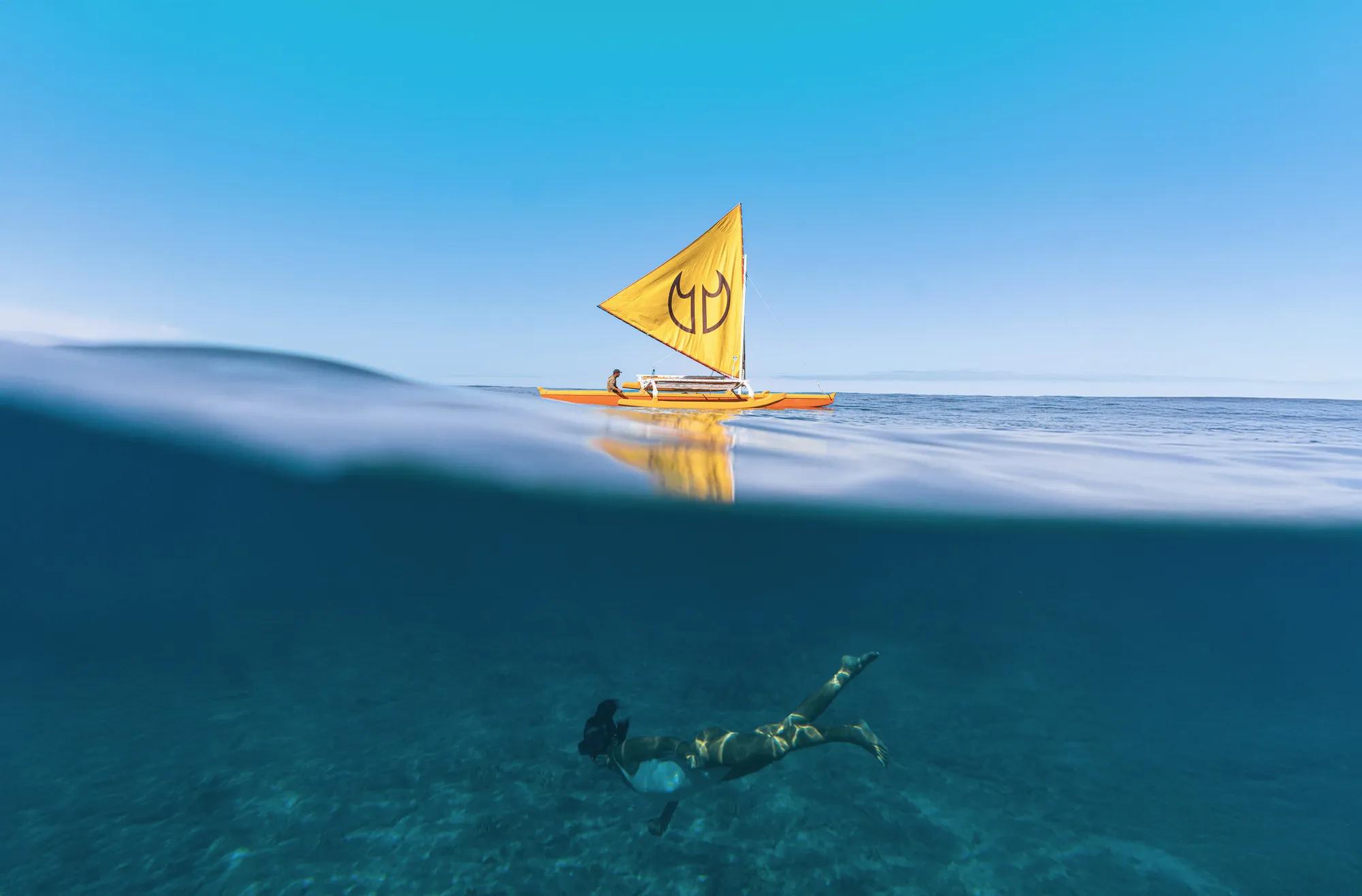 Underwater snorkeler with fins on swimming through clear blue water with boat on top of surface