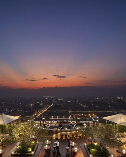 Rooftop bar at sunset with  city skyline views, white  umbrellas, and lounge  seating 