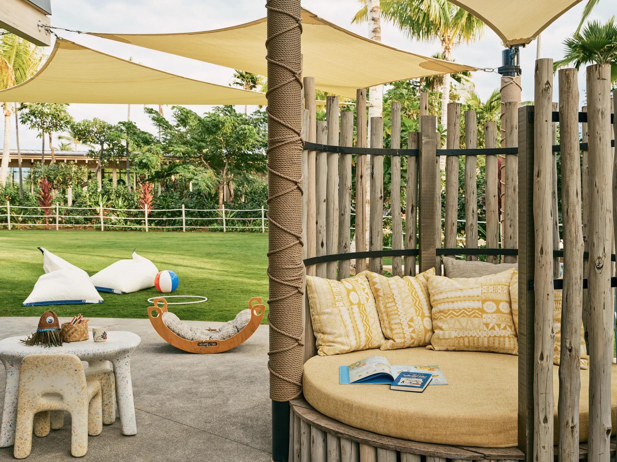 Outdoor playground / kids club with toys, games, bouncey ball, outdoor lounge area and shaded covering with palms in the distance
