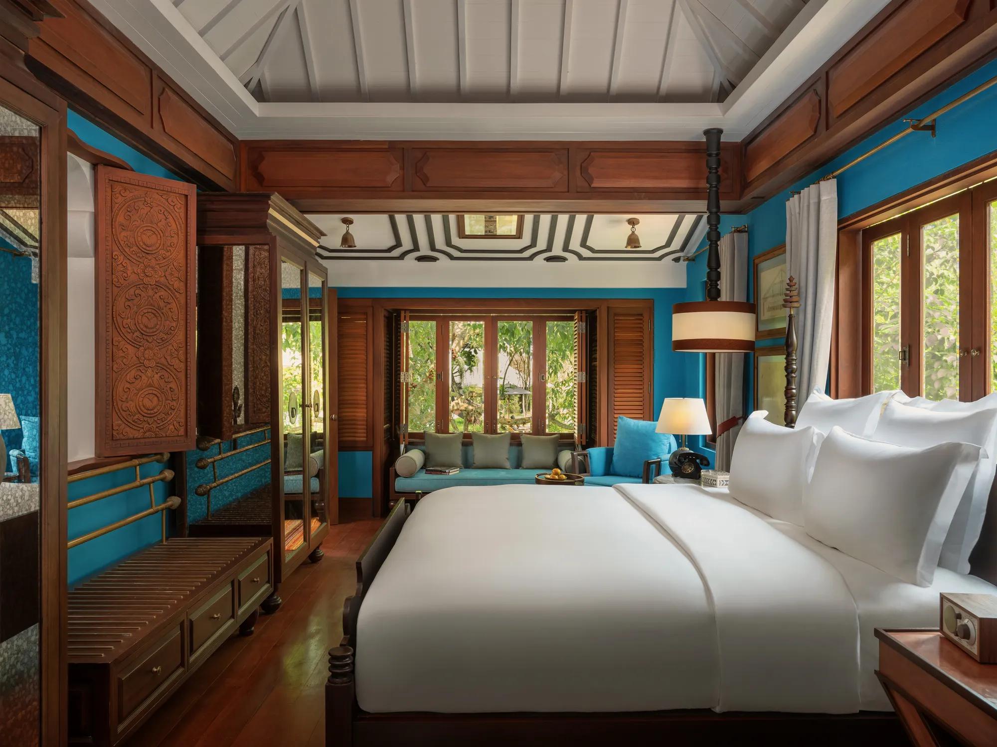 Luxury hotel bedroom in Luang Prabang with white bedding and turquoise walls.