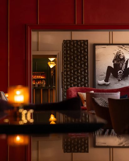 A lounge area decorated in rich reds, featuring patterned chairs, stylish tables, and a black-and-white photo on the wall.