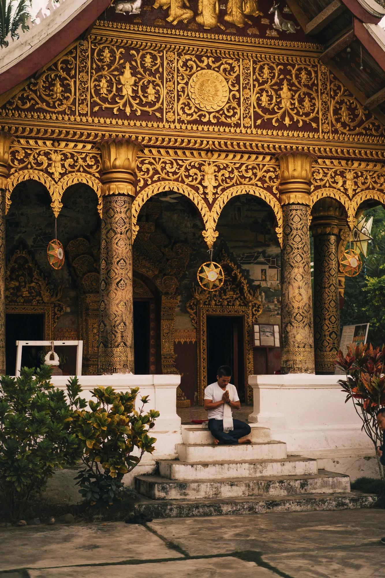 Person meditating on temple steps beneath an ornate gold-decorated archway.