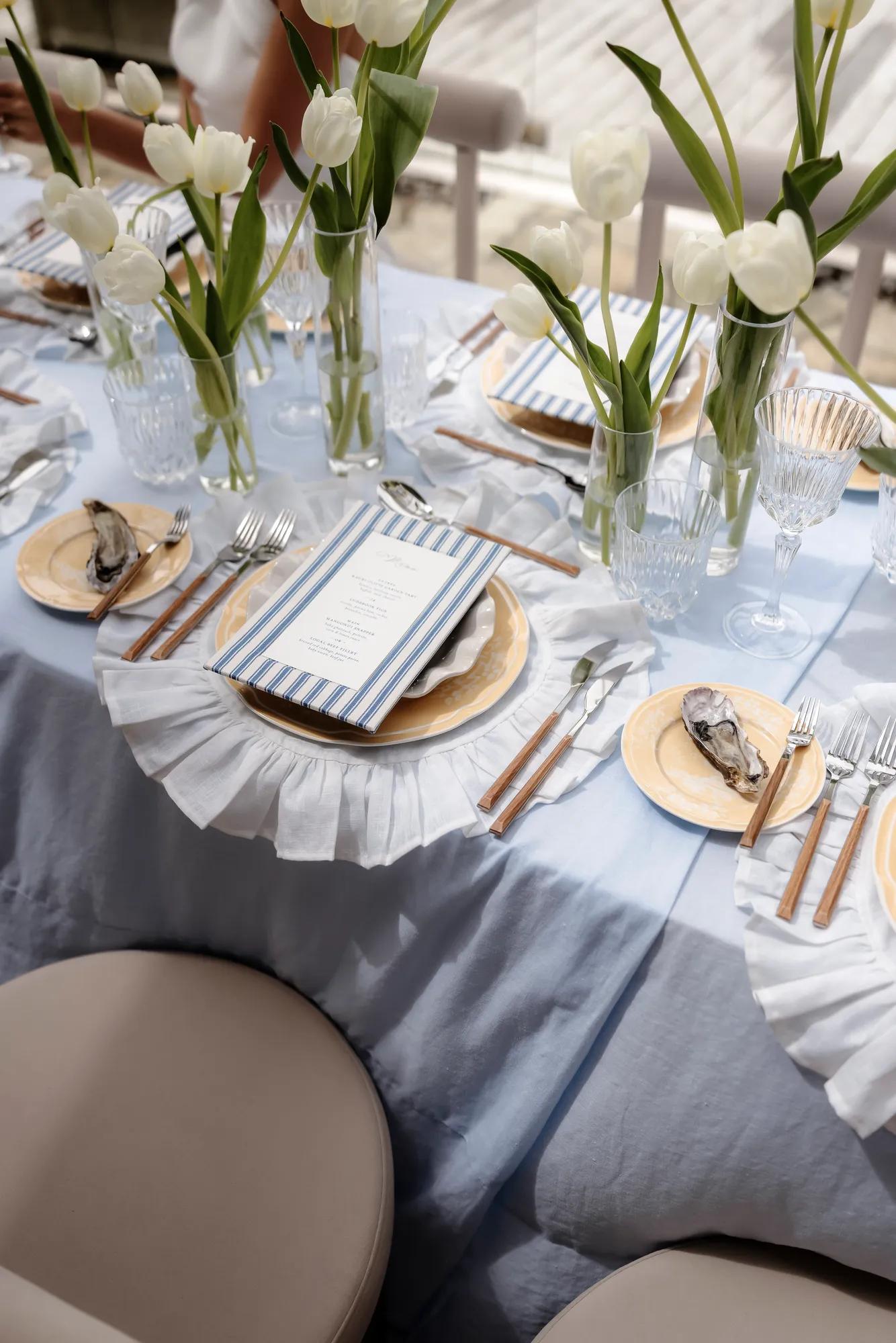 Intimate luxury villa wedding reception table with white tulips and yellow-blue coastal décor and a fresh oyster