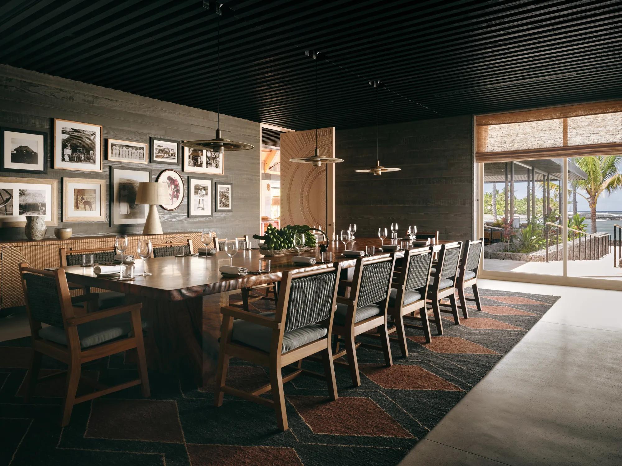 A private meeting room with a window looking out to the oean, and a  long rectangular table and chairs set with table settings and framed photographs along the wal.