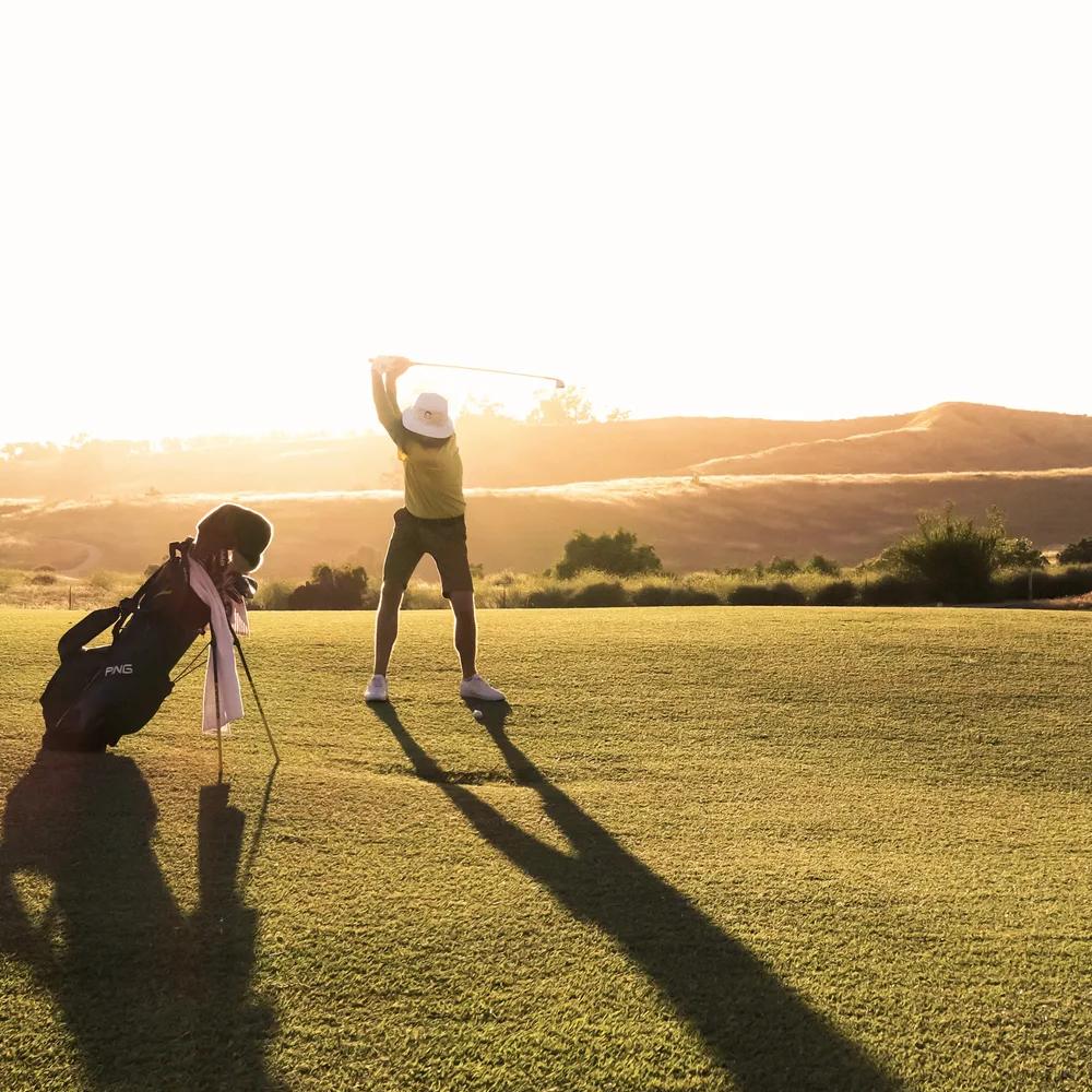 Sunset over a serene golf course, with a stylish man in a golf outfit enjoying the game, bathed in warm golden light