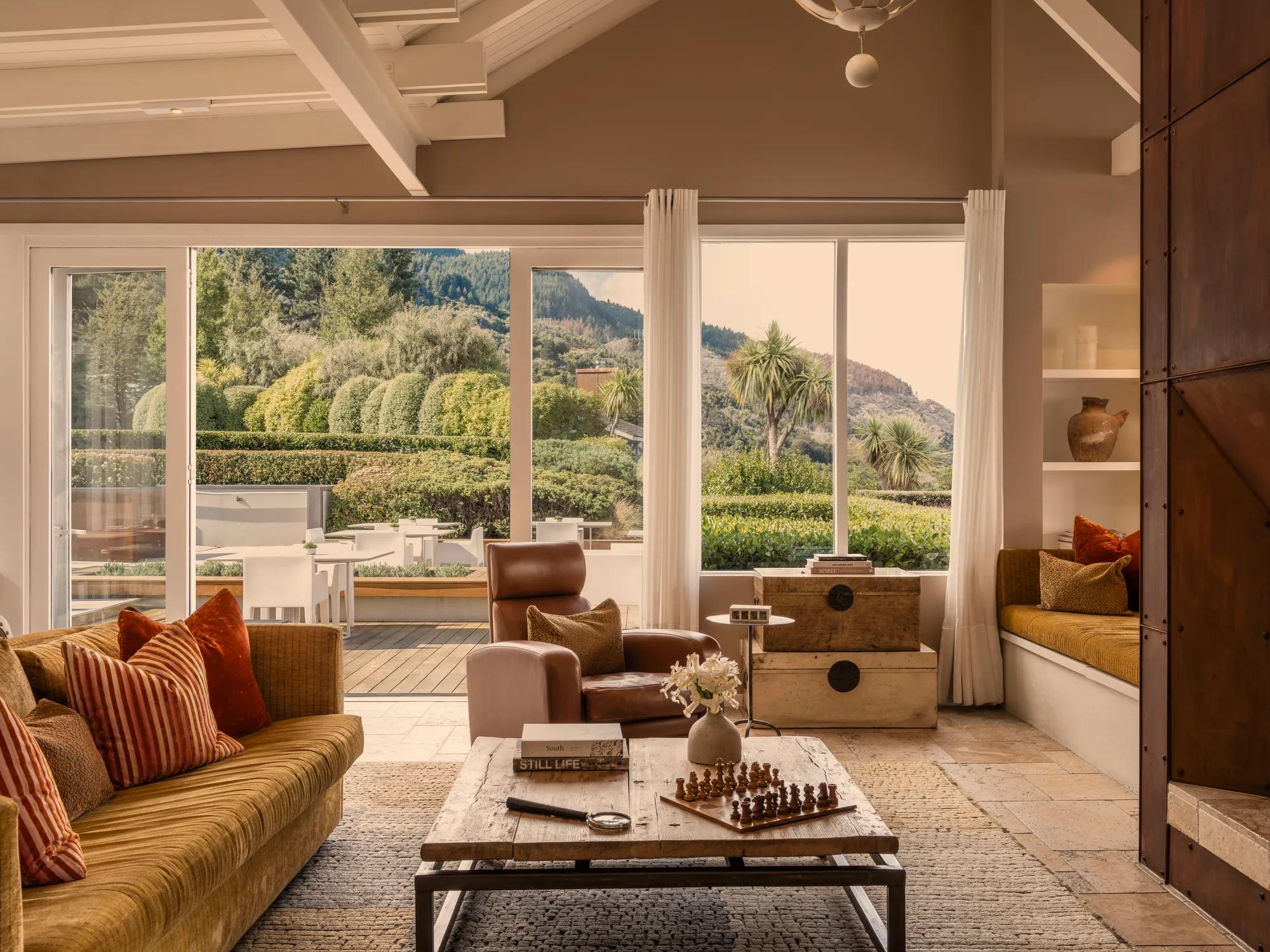 Lounge area at Rosewood Matakauri with luxury furnishings, Corten steel fire and open doors to a sunny terrace. 