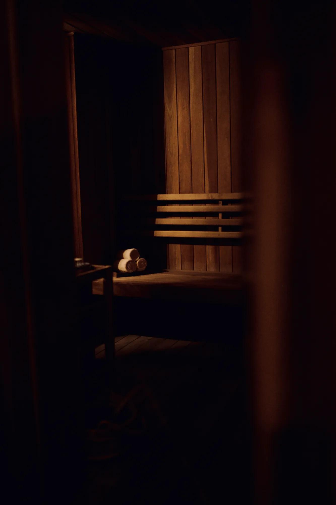 A wooden sauna with three rolled towels placed on the bench, softly illuminated by natural sunlight filtering in. 