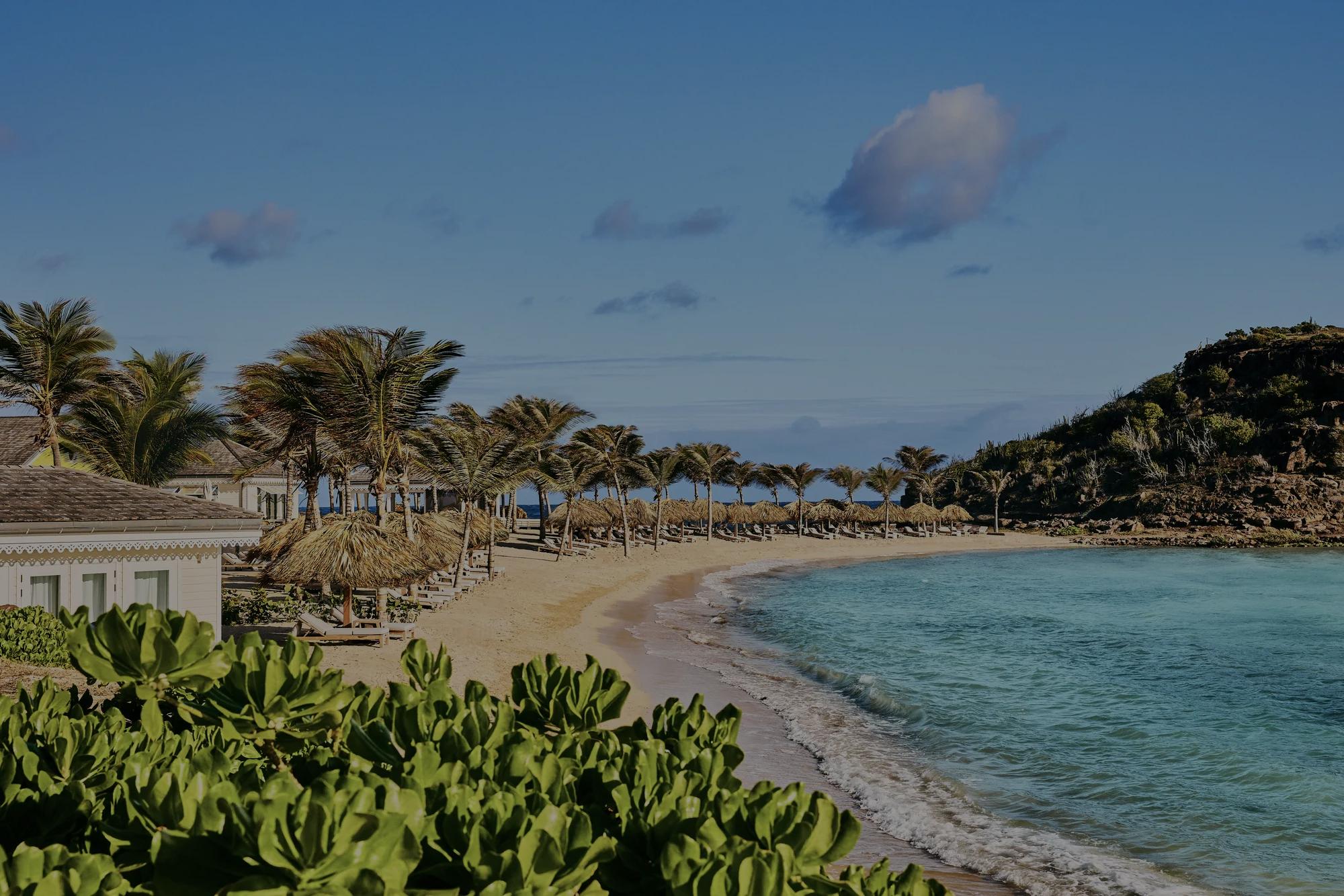 A view of a beach in St. Barth, showing multiple properties and a mountain in the background.