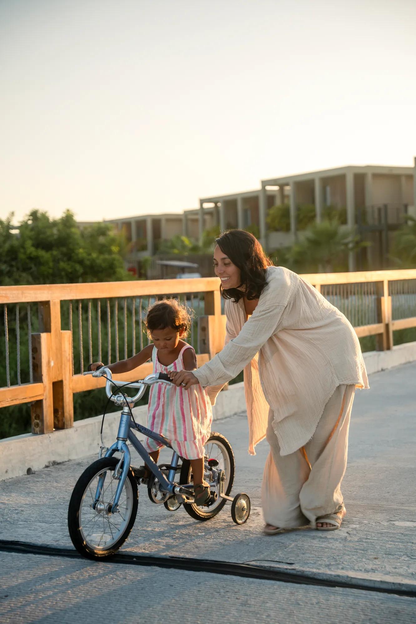 mom assisting daughter ride the kid's bicycle
