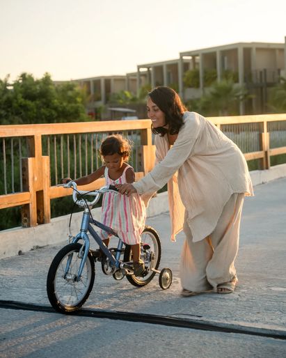 mom assisting daughter ride the kid's bicycle