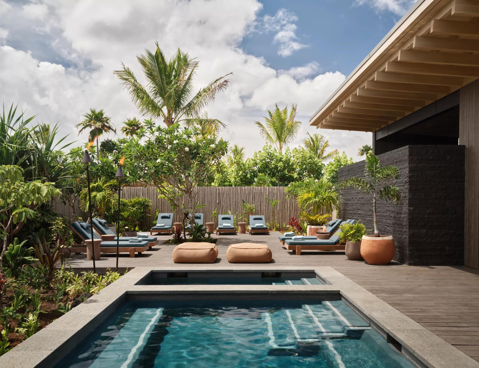 Outdoor spa lounge area with plunge pools, lounge chairs and seating surrounded by lush vegetation